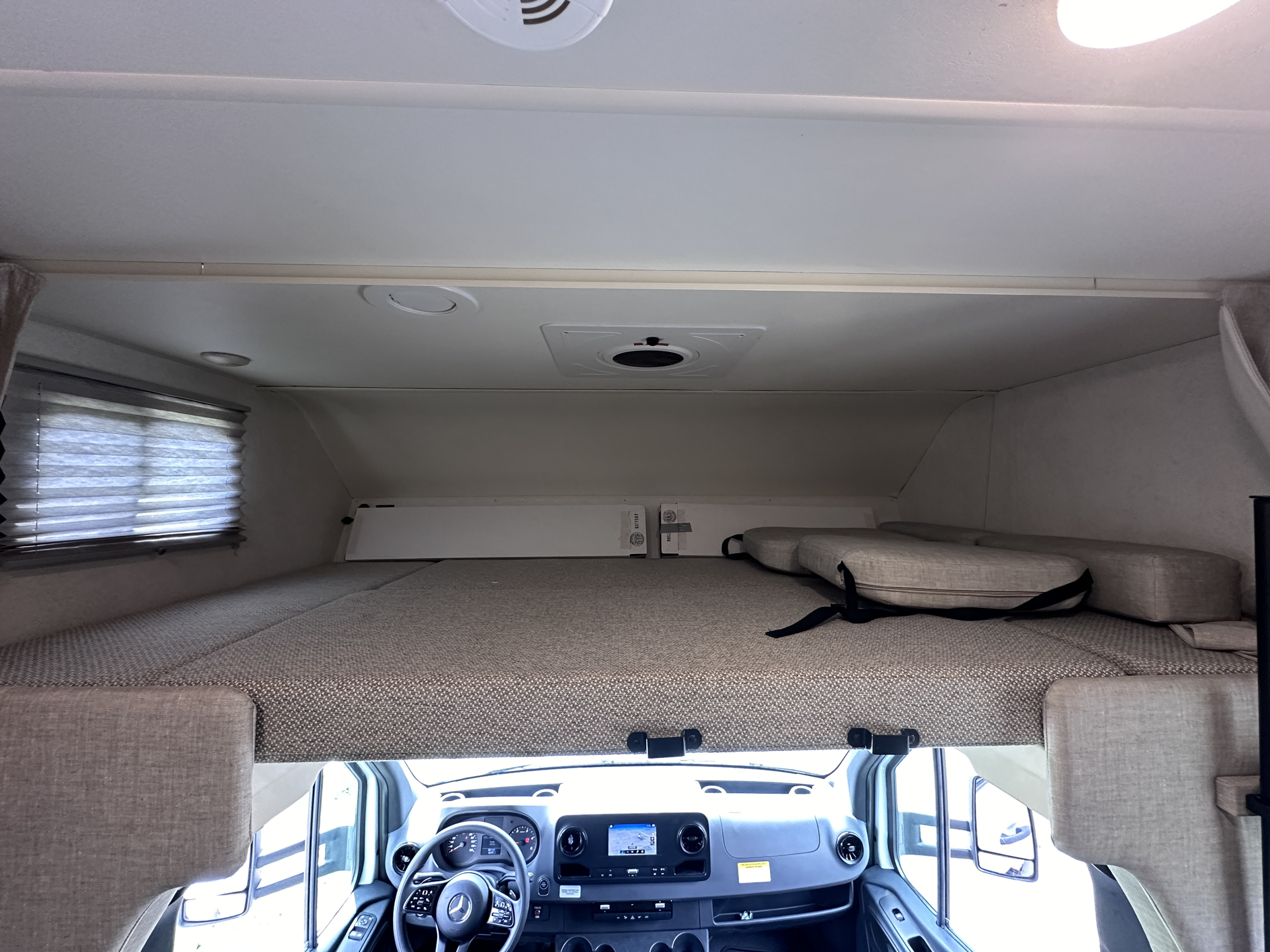 Inside an RV rental: view of the cab-over bunk with cushions and the Mercedes-Benz cockpit.. Winnebago Vita 2020