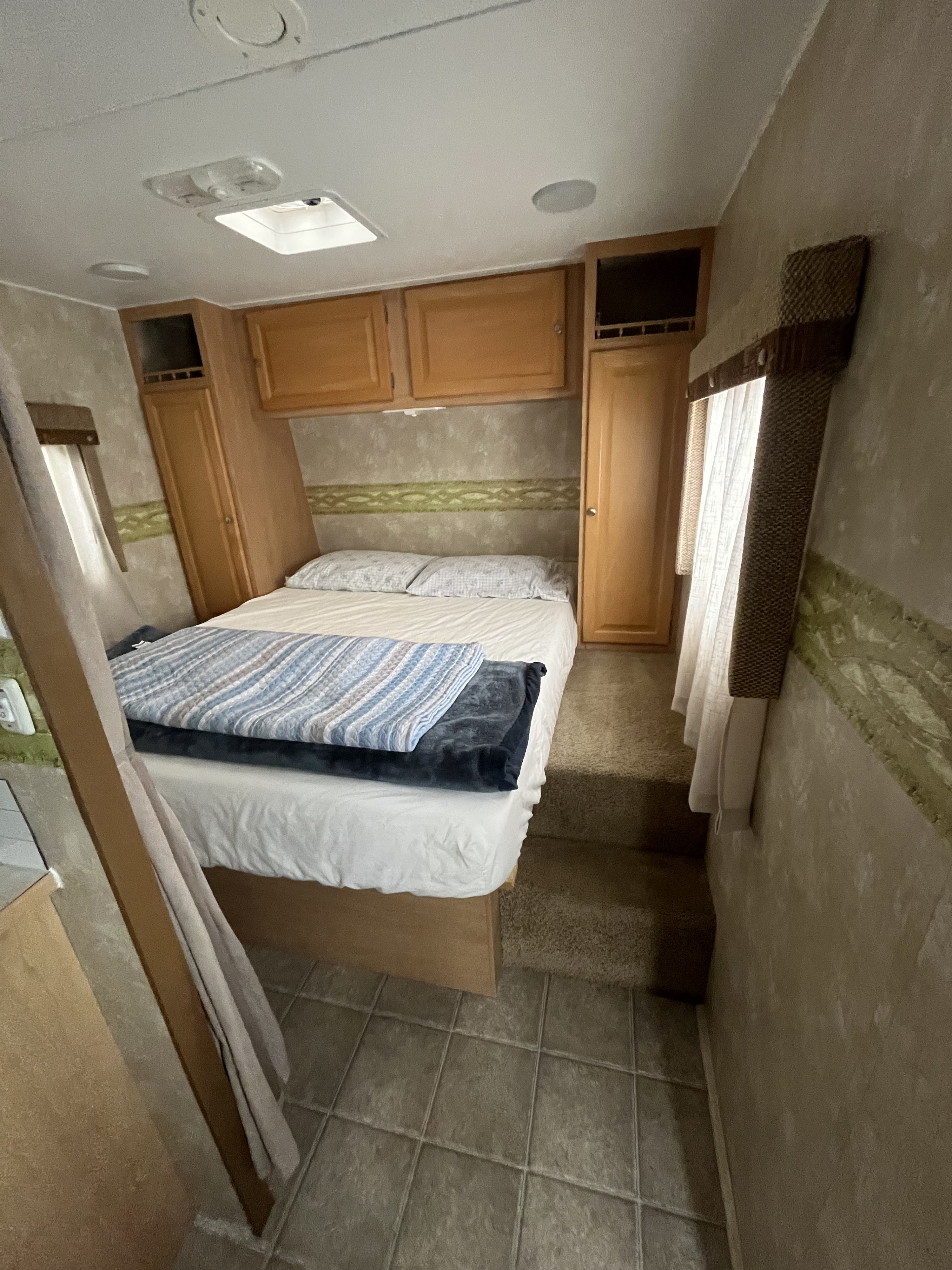 Cozy RV rental bedroom with a comfortable bed, wood cabinets, and windows, designed for comfort during travel.. Thor Motor Coach Wave 2007