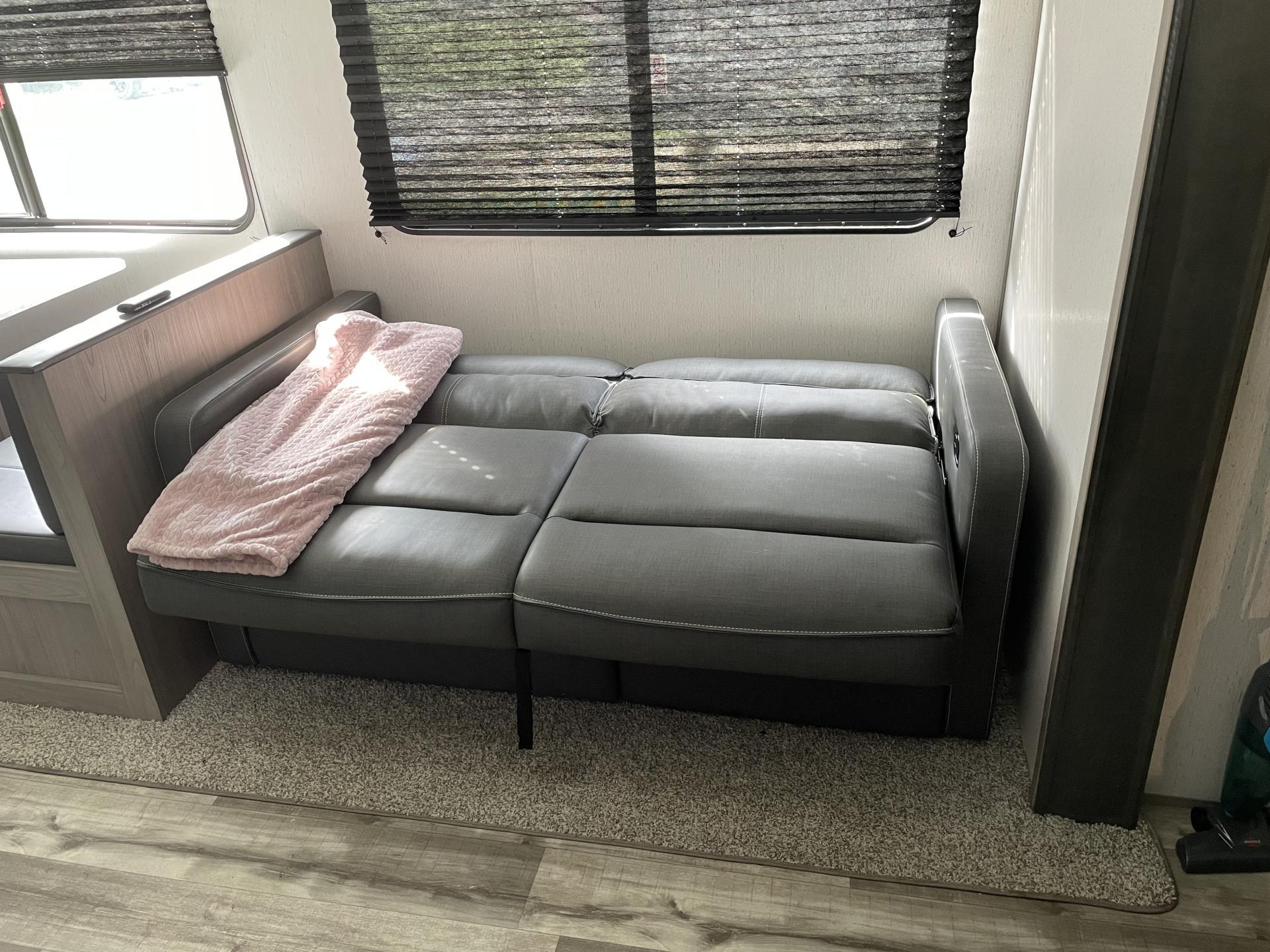 A cozy gray sofa/futon with a pink blanket inside an RV rental, offering a comfortable spot for your travel adventures.. Coleman Lantern 2022
