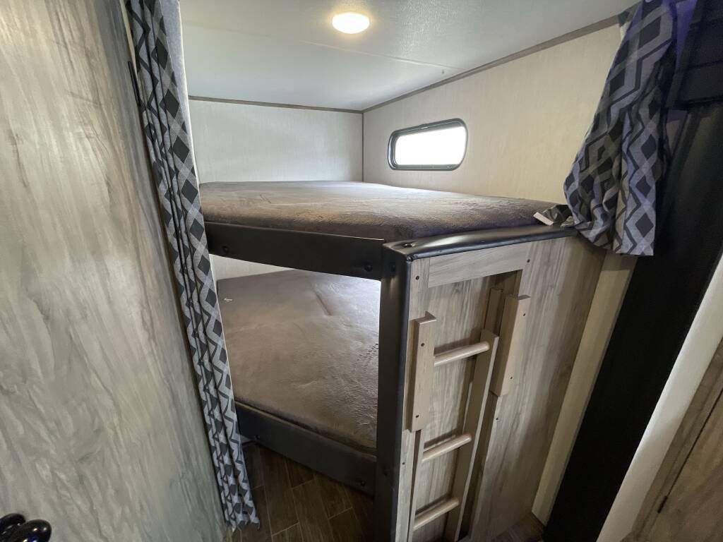 Compact RV rental interior featuring two comfortable bunk beds with a ladder and a small window. Ideal for family trips.. Forest River Cherokee Alpha Wolf 2022