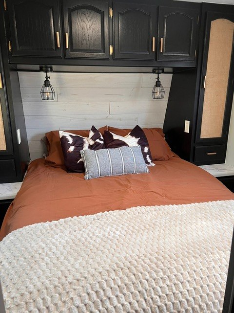 Modern RV rental bedroom featuring rust bedding, cowhide pillows, and black overhead cabinets with task lighting.. Wildcat Wildcat Trailer 2004