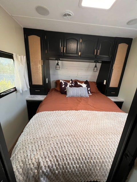 Cozy RV rental bedroom features a bed with rust & cream bedding, black cabinets, and modern lighting.. Wildcat Wildcat Trailer 2004