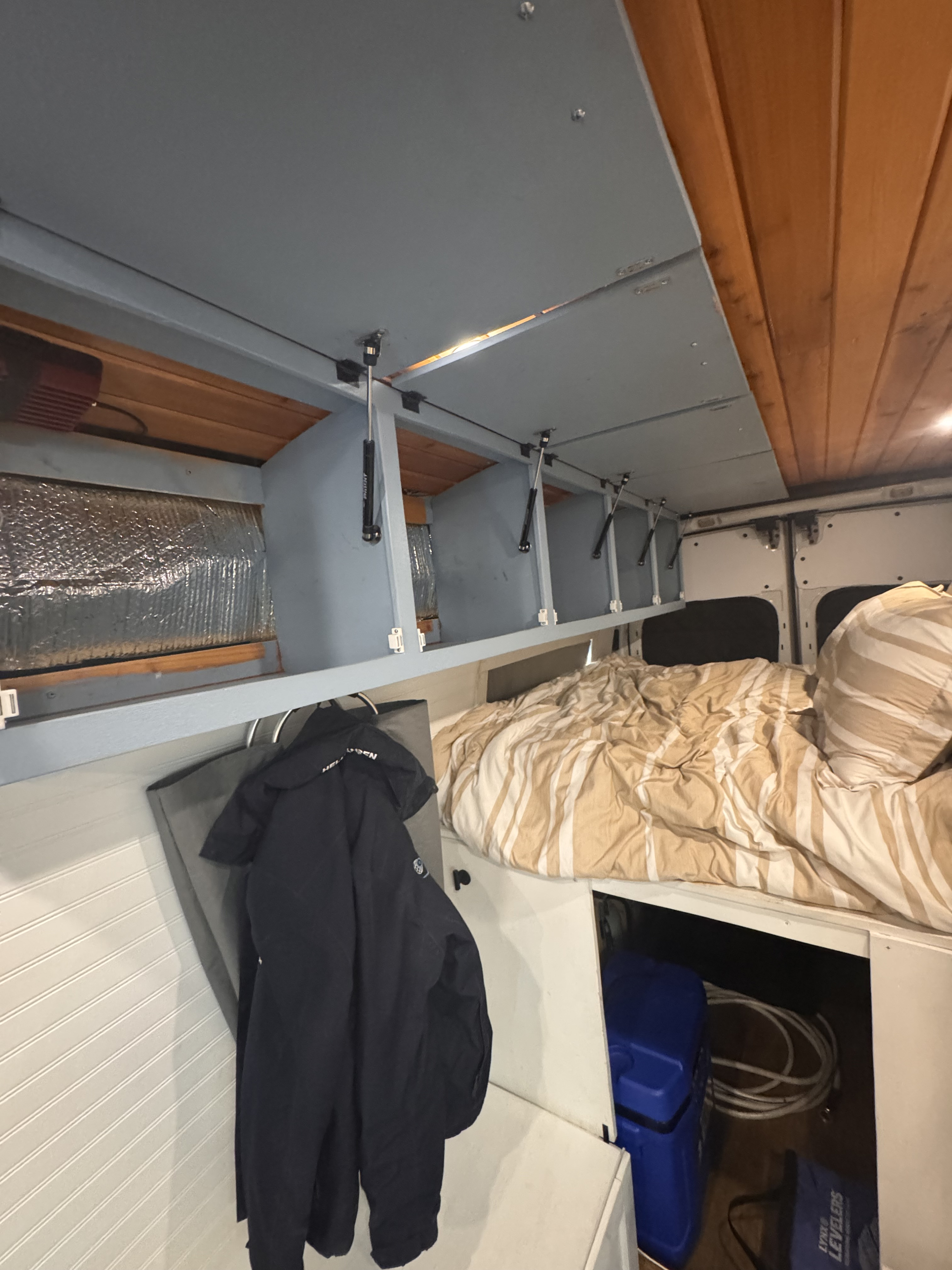 RV rental interior: A comfortable bed, open overhead cabinets with gas struts, and storage below. Ideal for travel.. Ford Van 2015