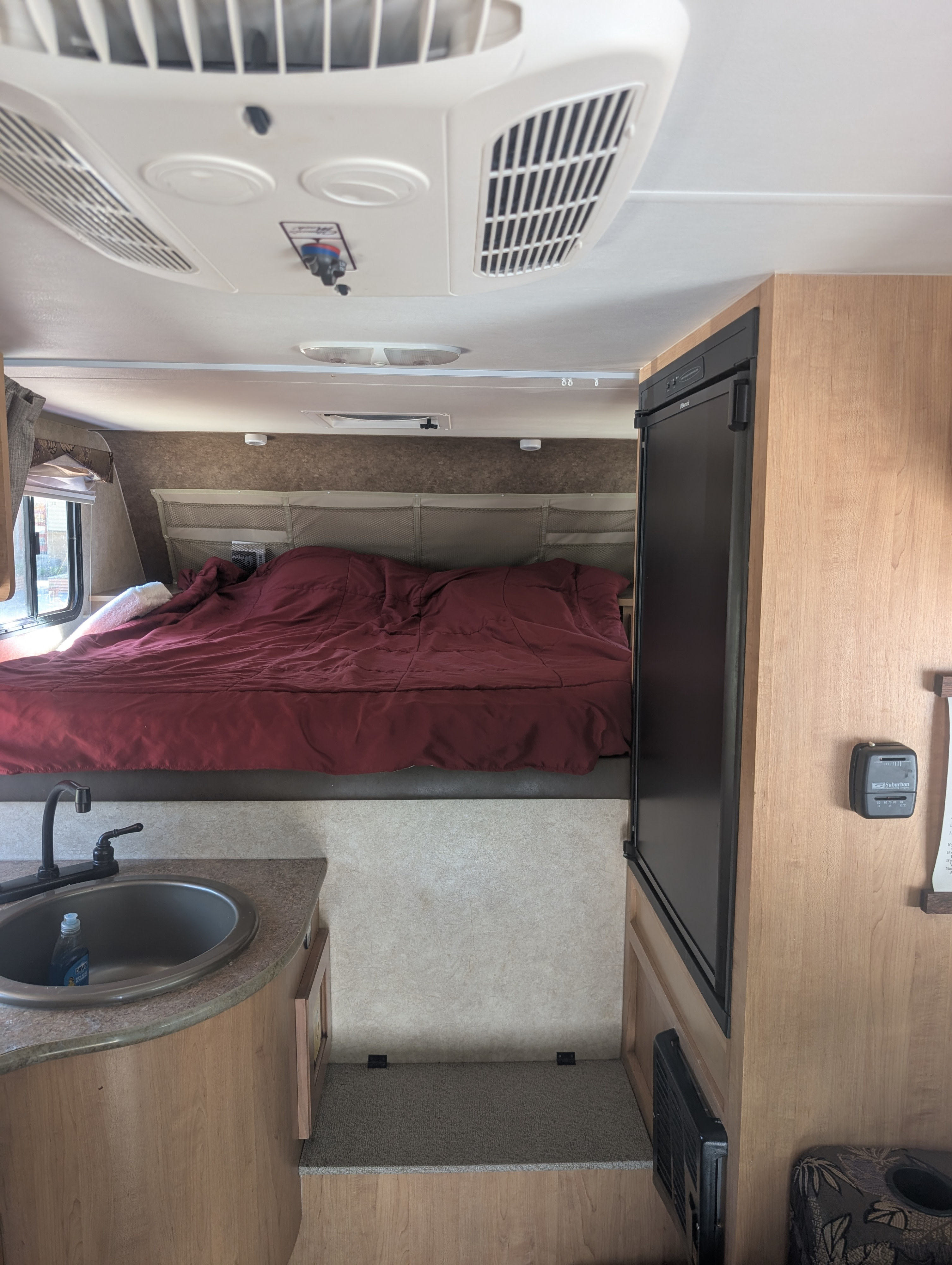 This RV rental interior shows a kitchen sink, cozy bed, and refrigerator, with an AC unit above. Compact and functional.. Adventurer Adventurer 2015