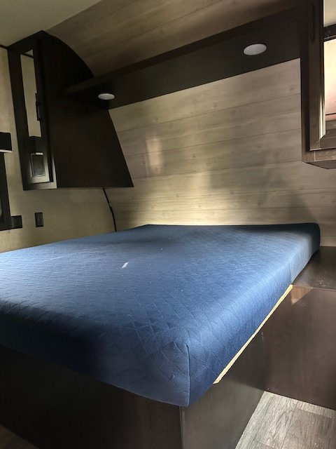 This RV rental bedroom features a comfy blue mattress, wood-paneled wall, and dark storage units with lights.. Jayco Jay Flight 2022