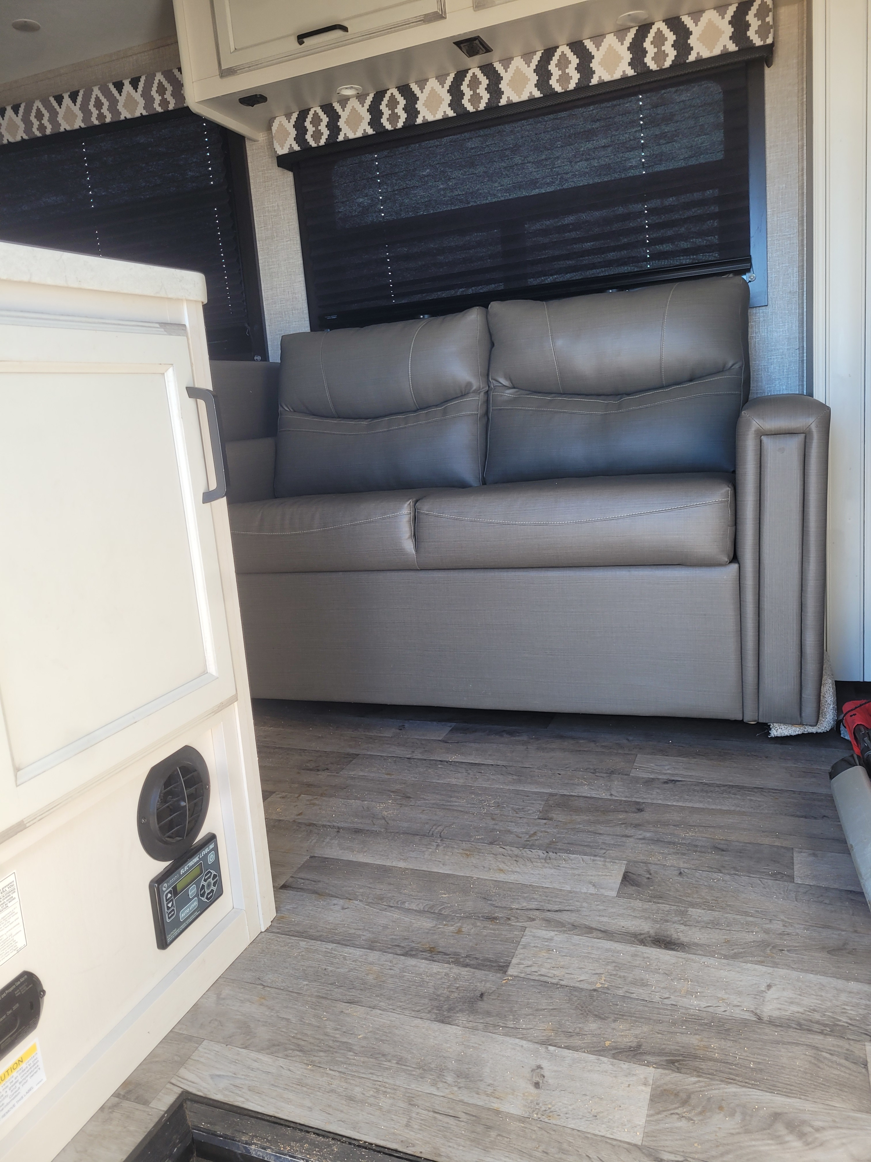 Modern RV rental interior with a gray sofa, decorative window valances, and wood-look flooring.. Jayco Redhawk 2022