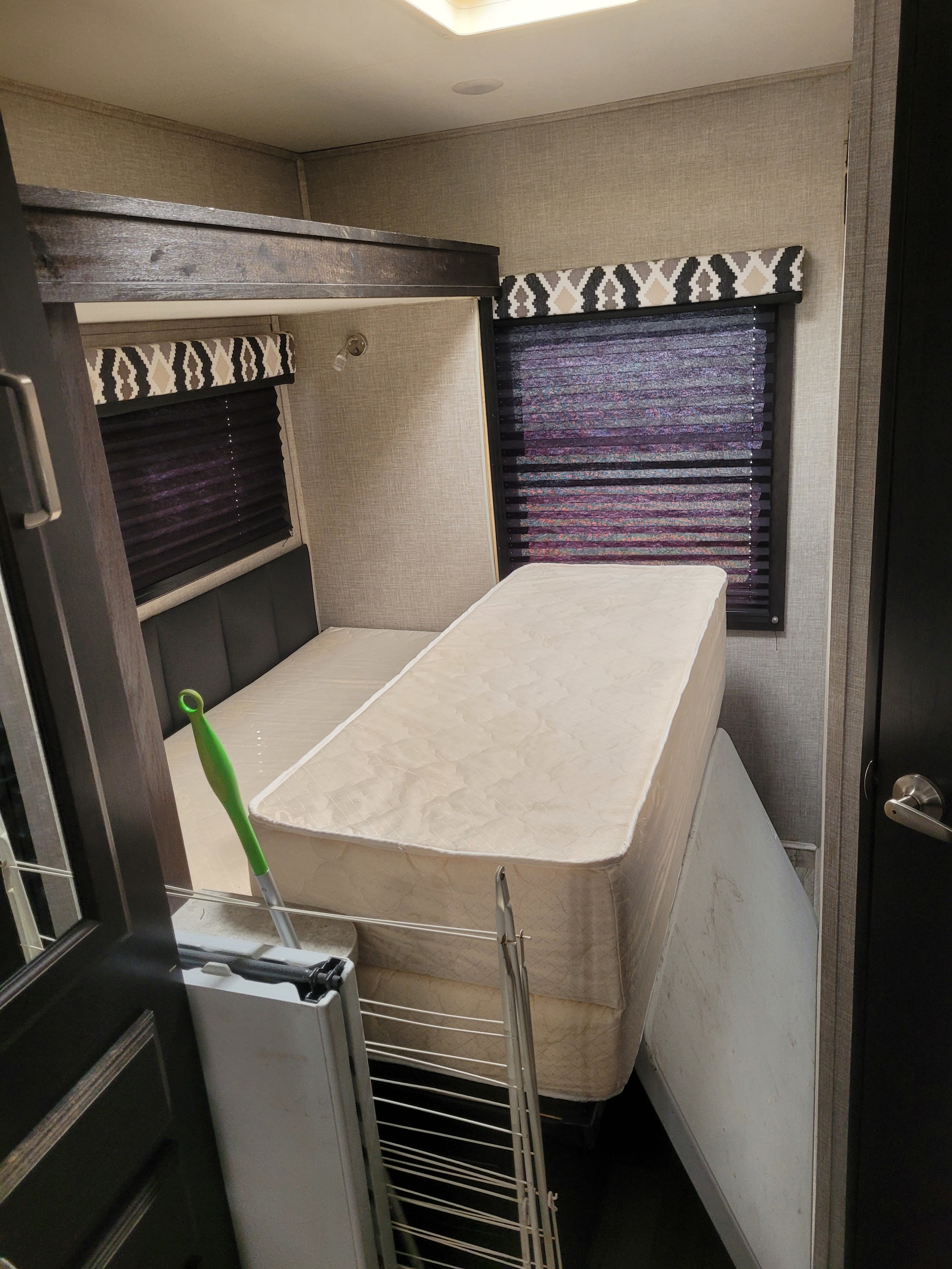 Inside an RV rental: a compact bedroom with bunk beds, dark blinds, and a mattress propped up.. Jayco Redhawk 2022