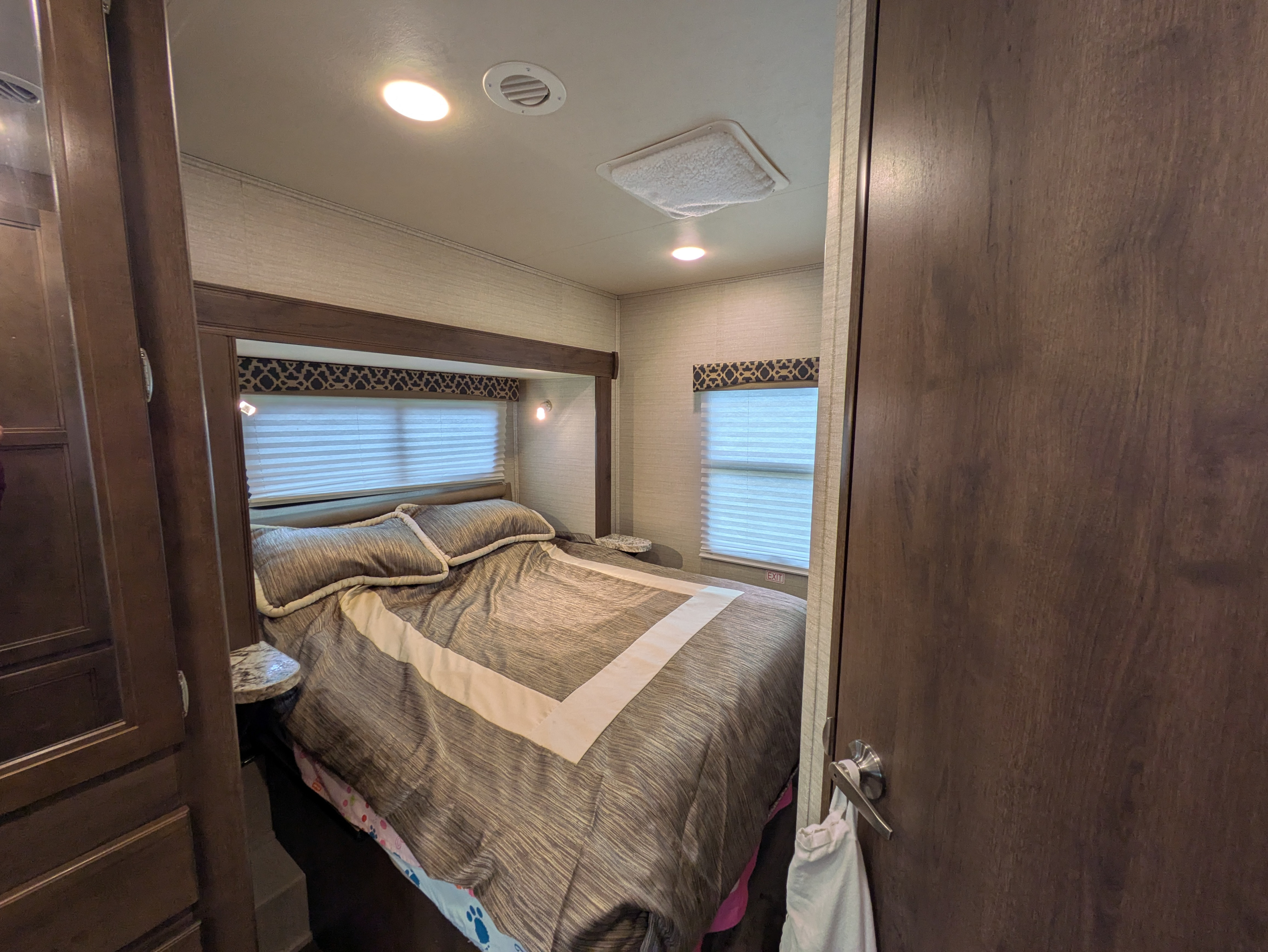 Cozy RV rental bedroom featuring a comfortable bed, two windows with blinds, built-in storage, and bright overhead lighting.. Jayco Redhawk 2021