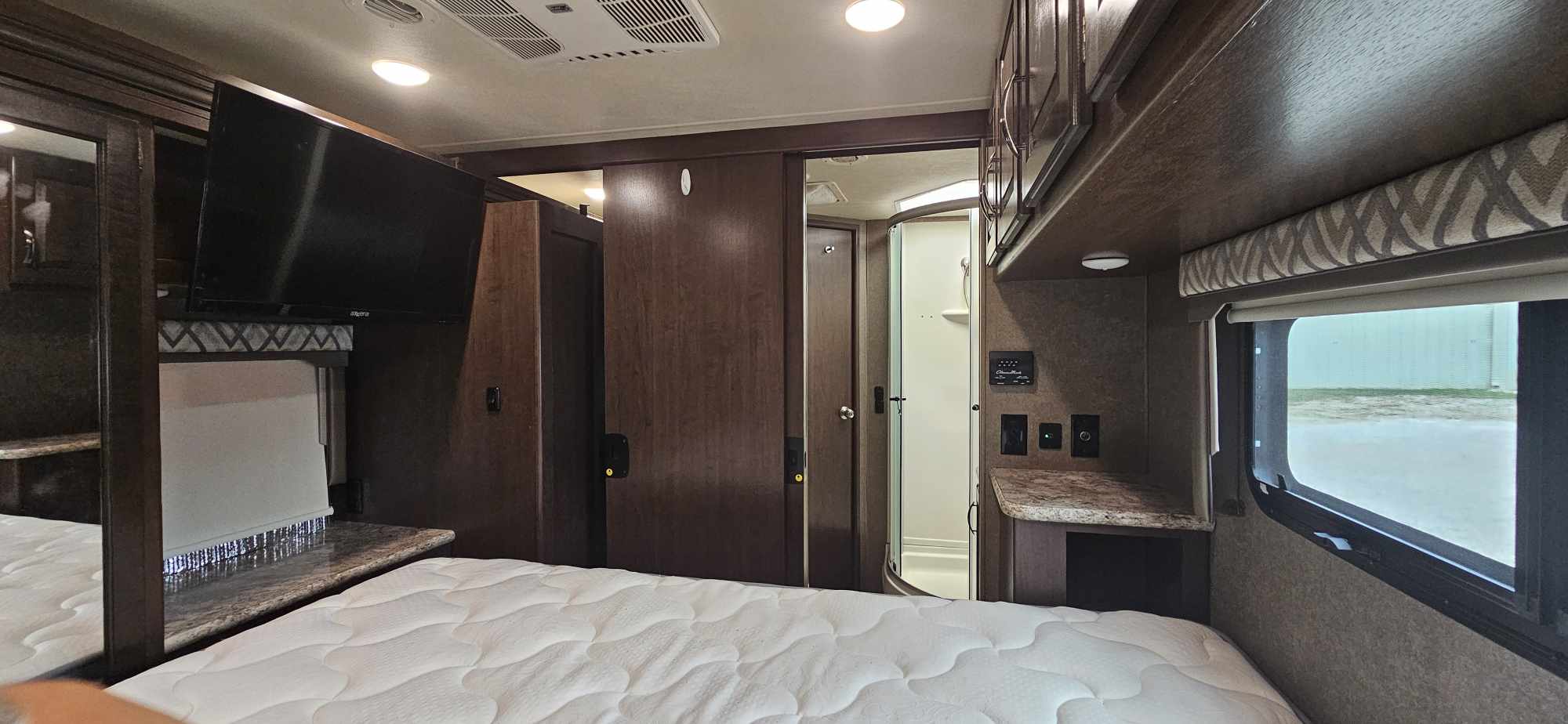 Spacious RV rental bedroom with comfortable bed, mounted TV, storage, and access to a full bathroom/shower.. Thor Four Winds 2020