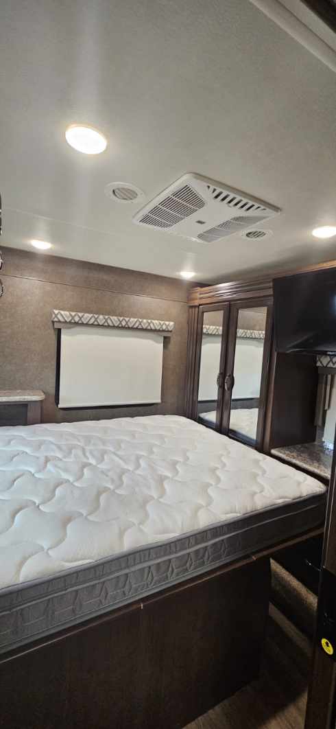 Spacious RV rental bedroom featuring a comfortable mattress, mirrored closet, and ceiling AC unit for a cozy travel experience.. Thor Four Winds 2020