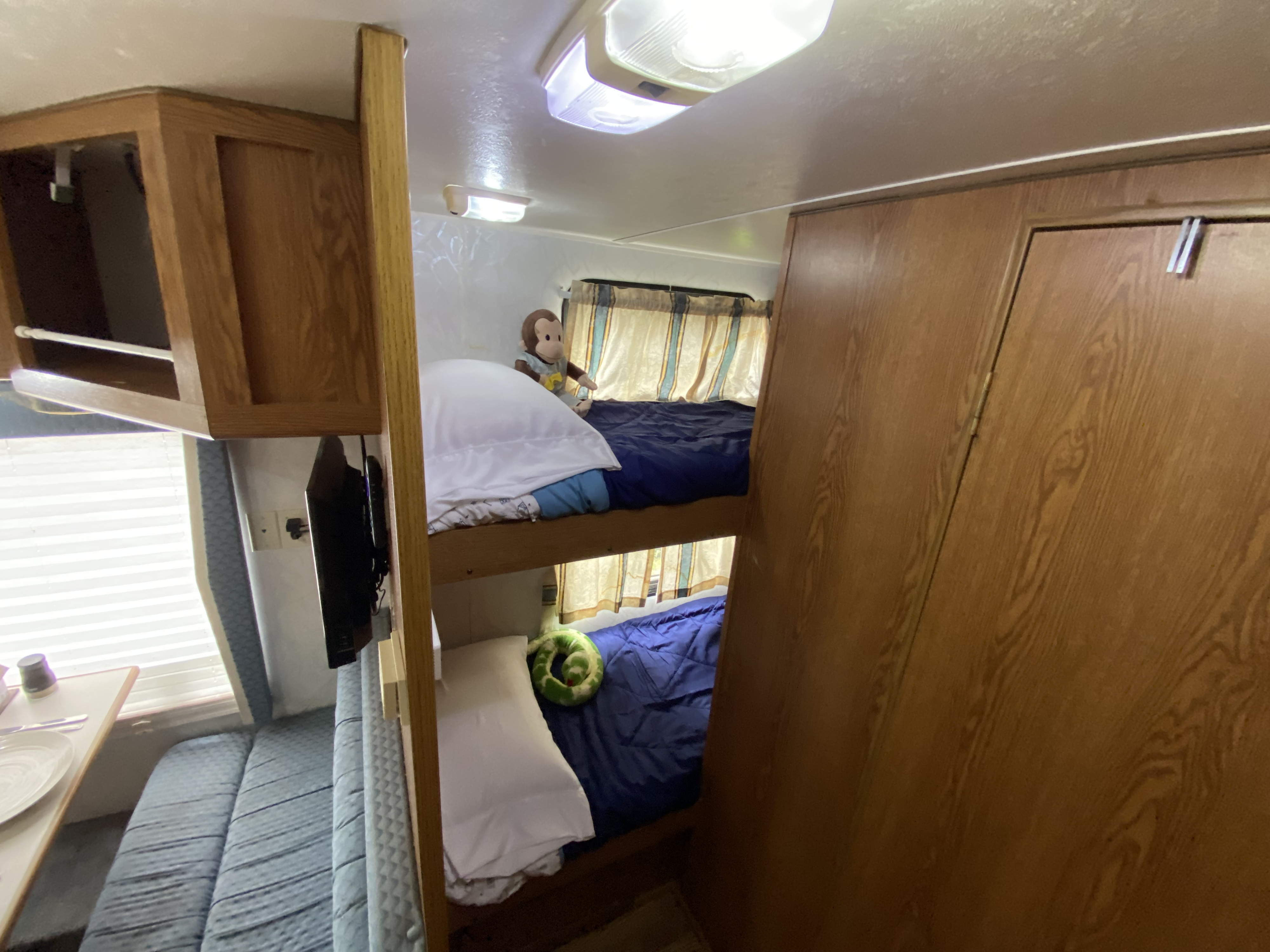 Cozy RV rental interior featuring wooden bunk beds, a dining area with blue seating, and mounted TV.. Holiday Rambler Alumascape 1998