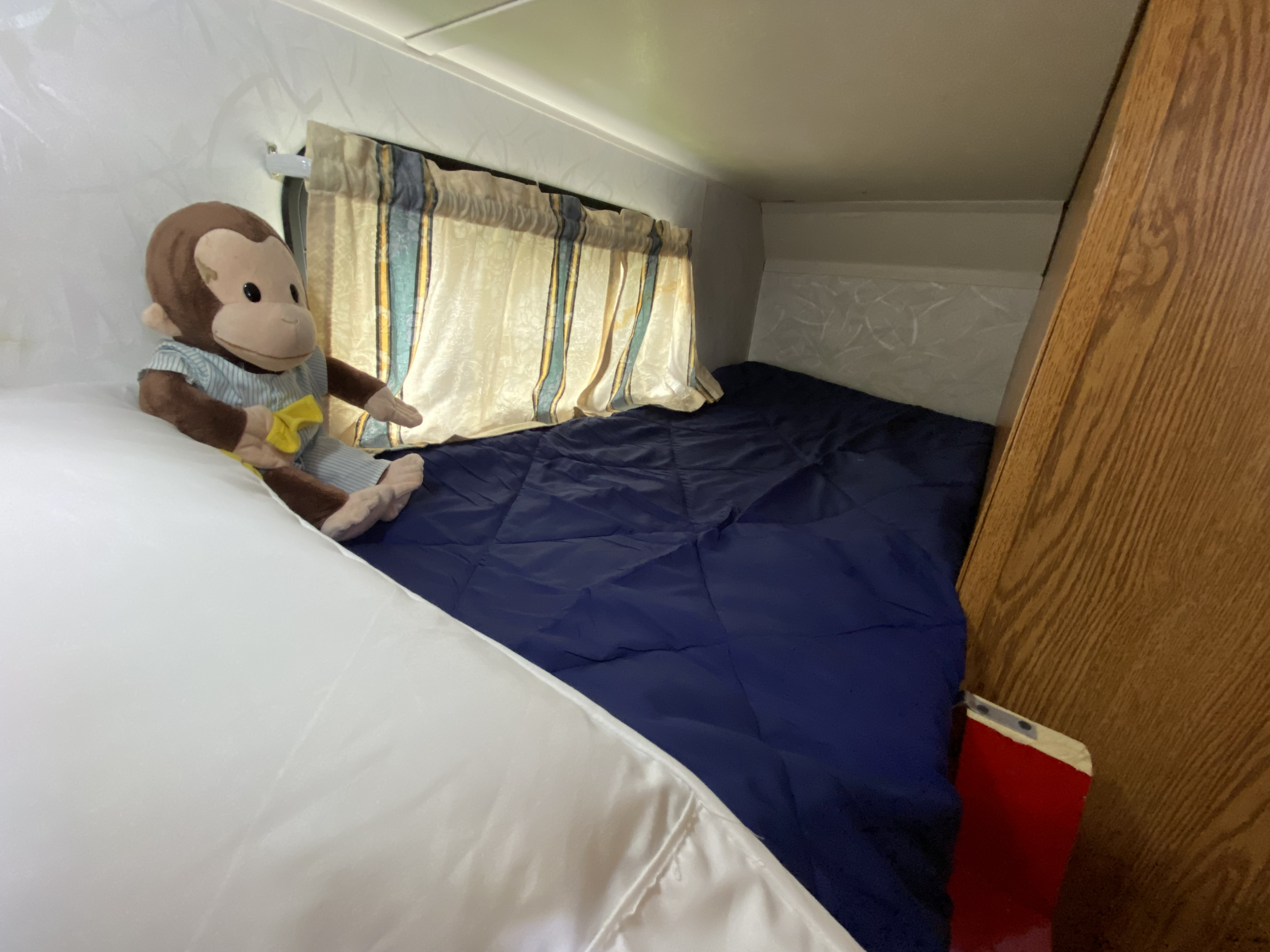Cozy RV rental sleeping area: blue bed, striped curtains, and a Curious George plush.. Holiday Rambler Alumascape 1998