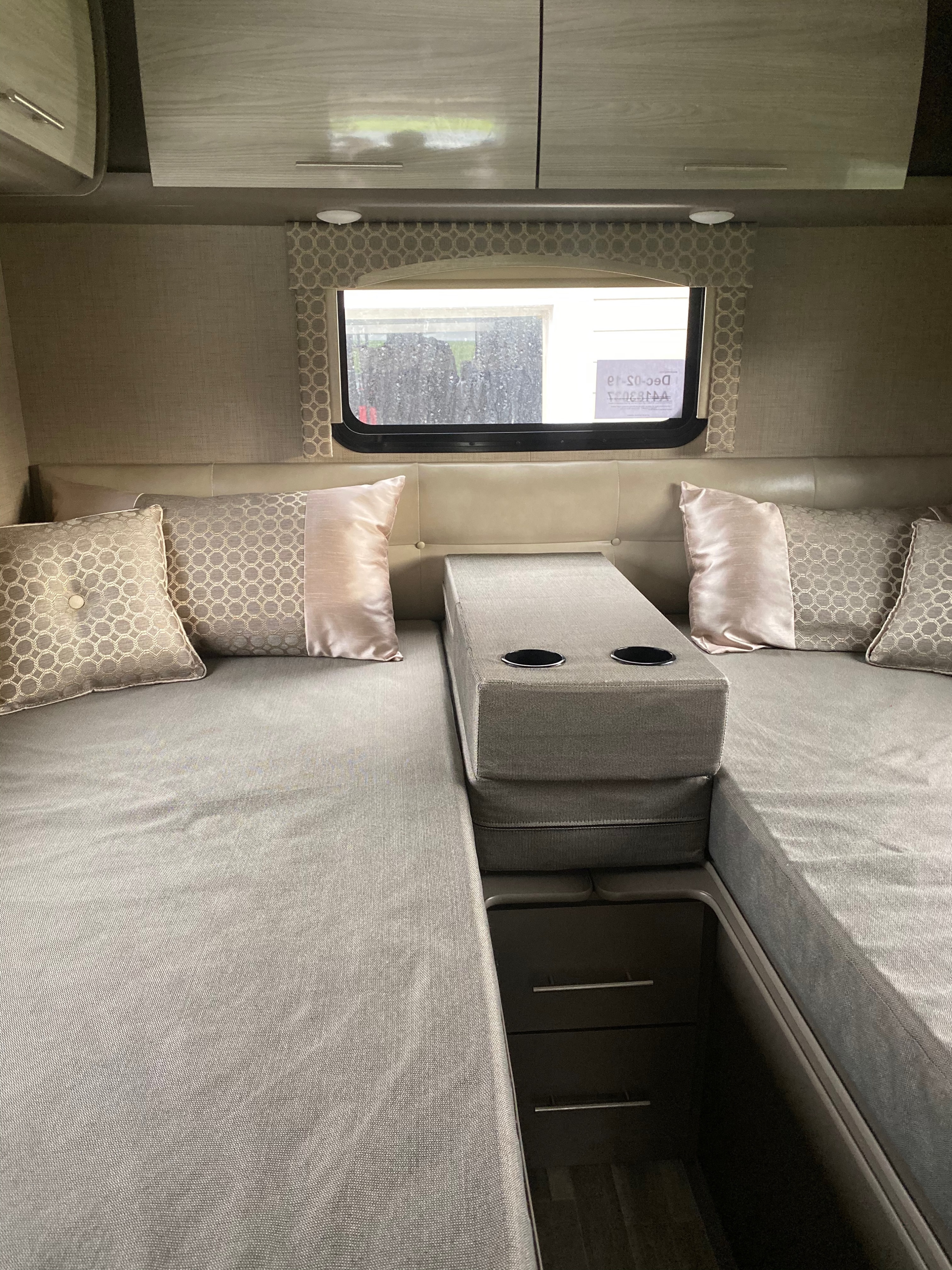 Inside an RV rental: a neutral-toned interior showing convertible beds/benches, accent pillows, and overhead storage.. Thor Axis 2019