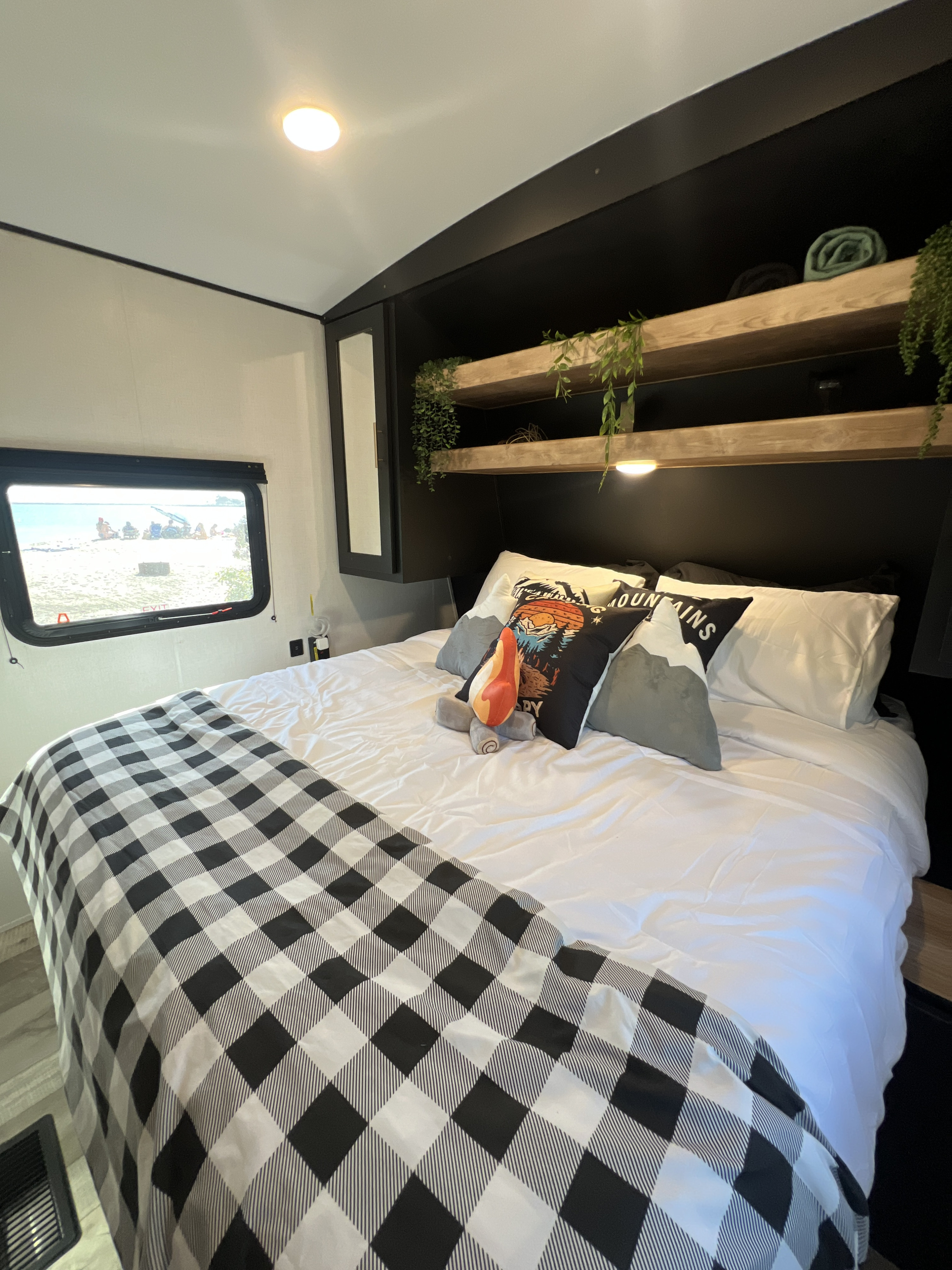 Cozy RV rental bedroom with a white bed, buffalo plaid blanket, mountain pillows, and a sunny beach view.. Keystone RV Springdale 2023