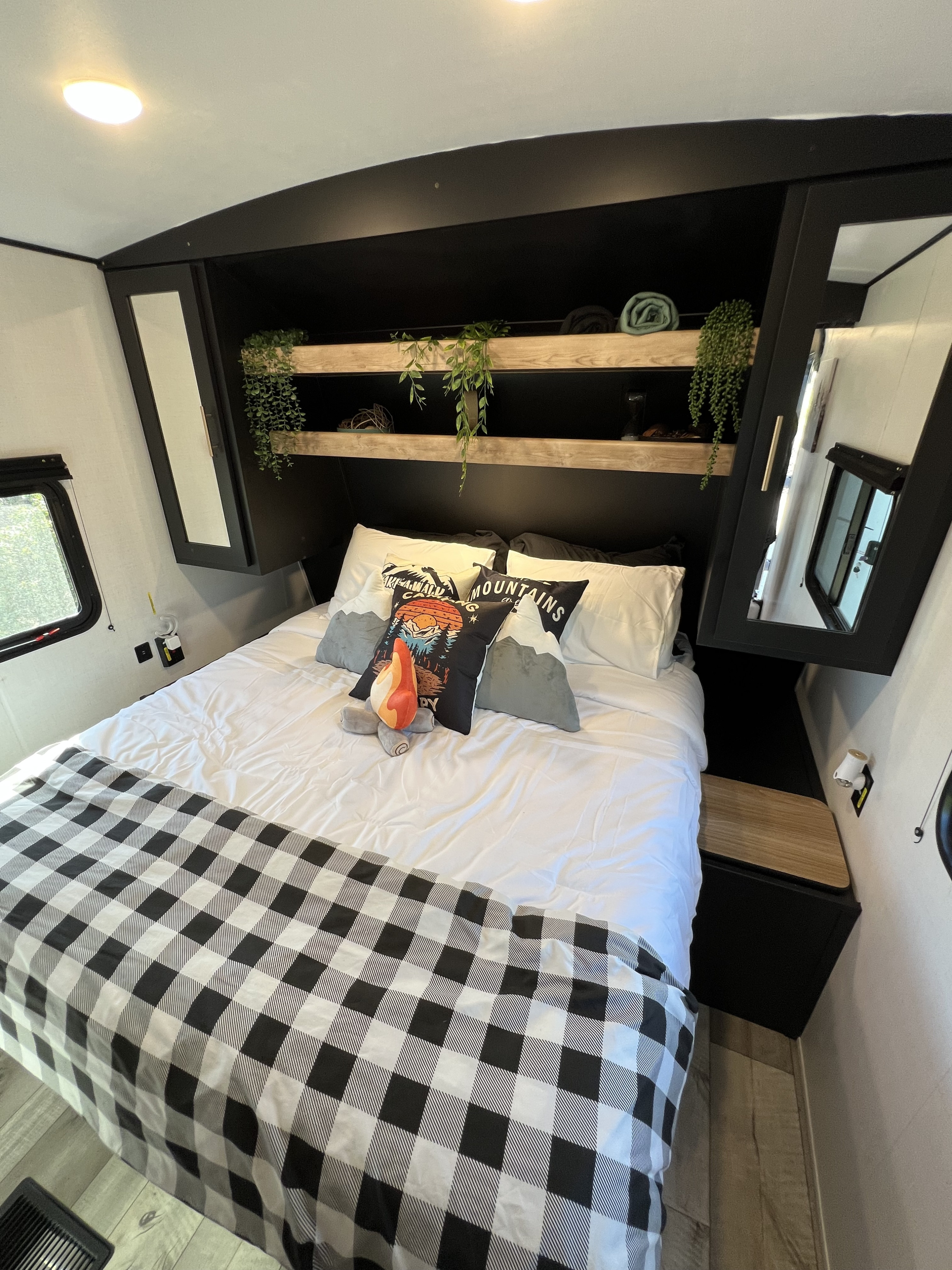 Cozy RV rental bedroom features buffalo plaid bedding, mountain-themed pillows, and overhead storage with shelves.. Keystone RV Springdale 2023