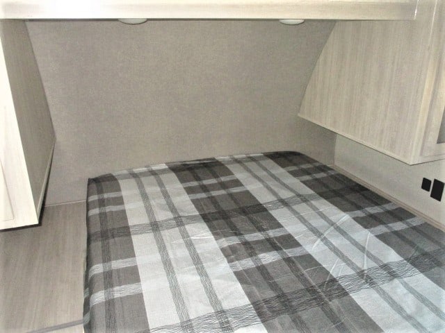 Compact RV rental bedroom featuring a bed with a gray plaid comforter, overhead lighting, and built-in storage cabinets.. Forest River Coachmen Catalina Legacy 2022