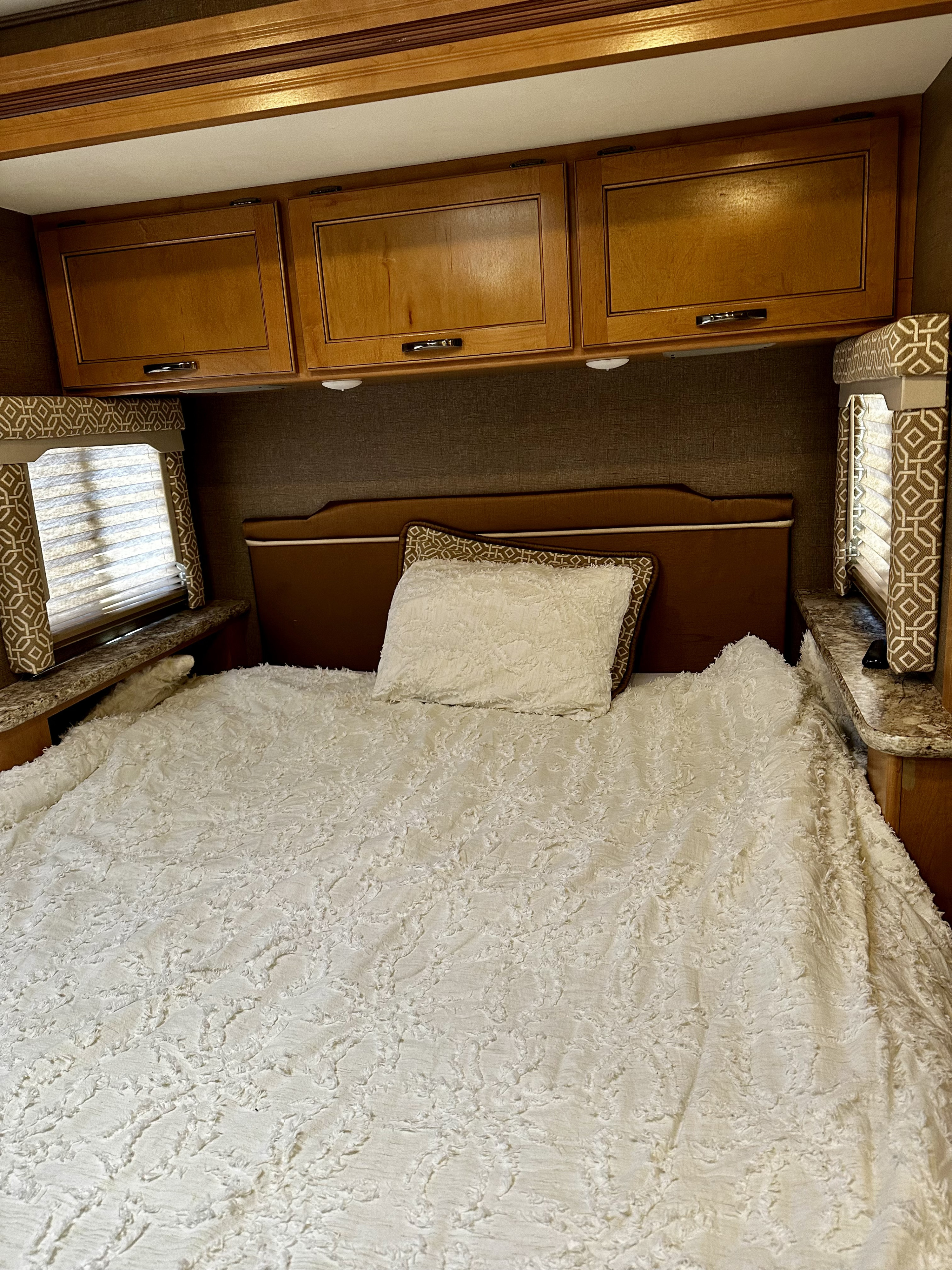 Experience comfort in this RV rental bedroom featuring a soft white textured bed, wood cabinets, and window treatments.. Thor Freedom Elite 2017