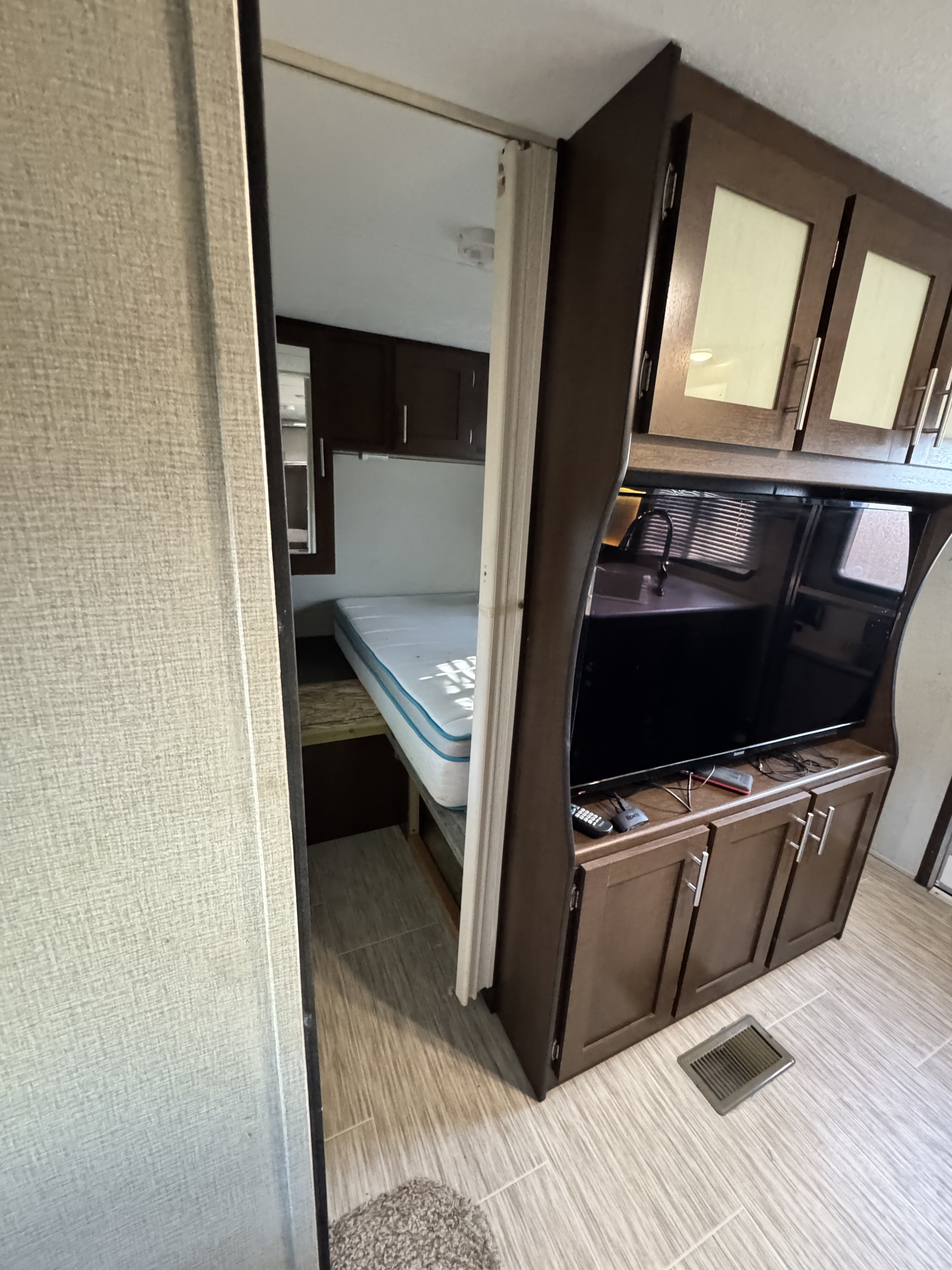 This RV rental interior highlights a bunk bed area and living space with a TV, kitchen sink, and storage.. Forest River Avenger ATI 2018