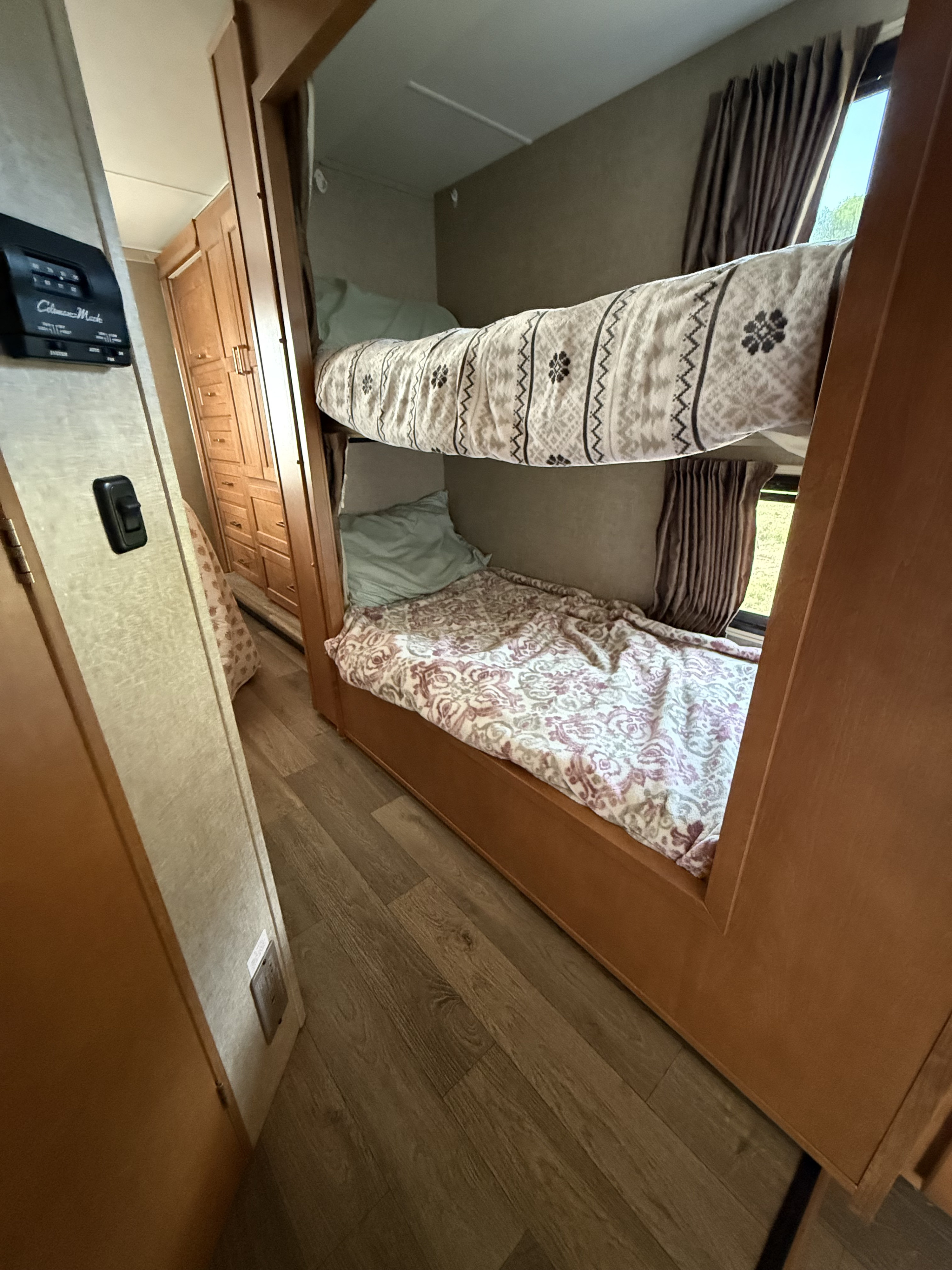 RV rental interior featuring cozy bunk beds with patterned blankets, a control panel, and wood cabinetry.. Winnebago Mini Winnie 2019