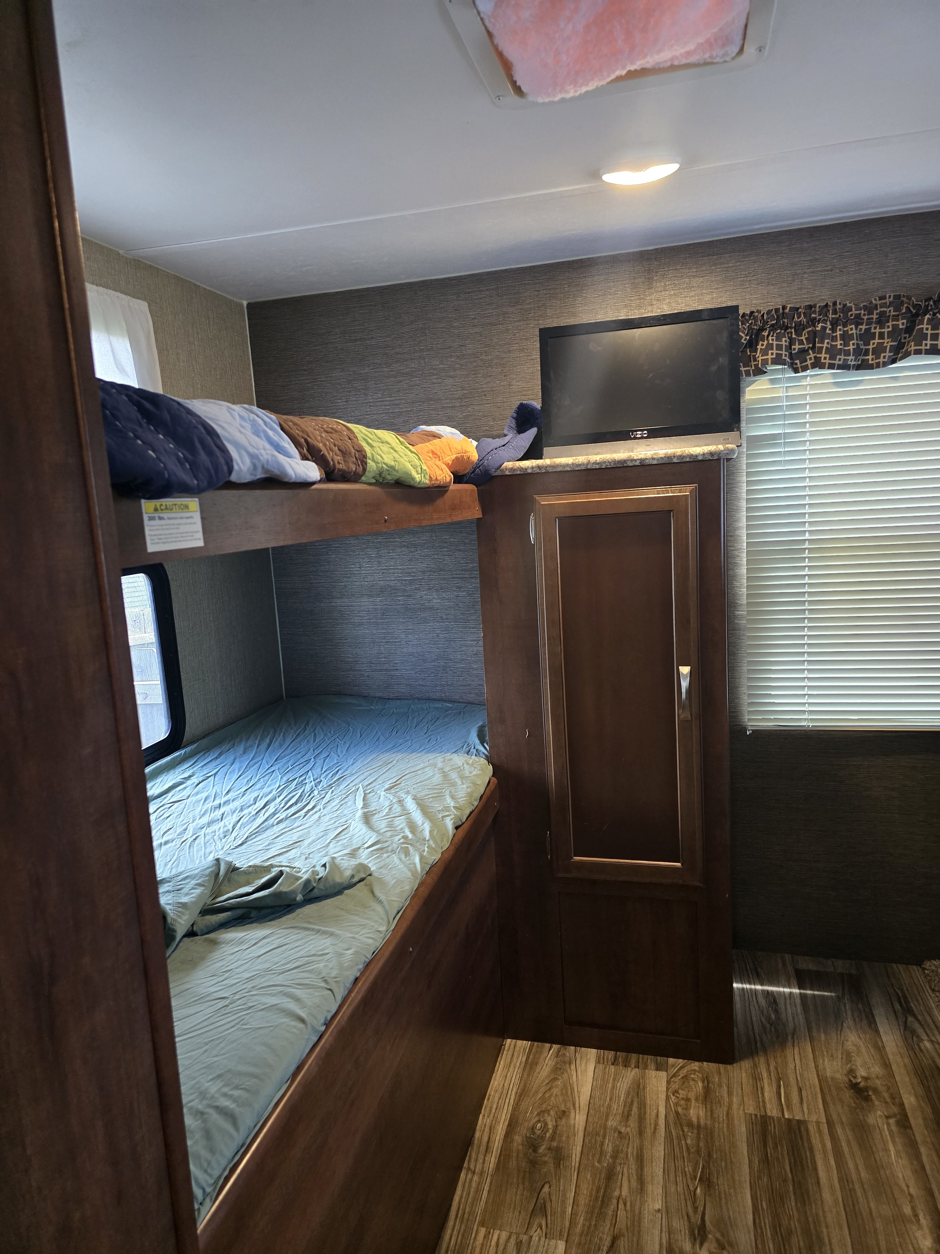 An rv rental's interior bunk beds, upper with colorful quilts and lower with blue sheets. Includes TV, window with blinds.. Keystone RV Passport Grand Touring 2017