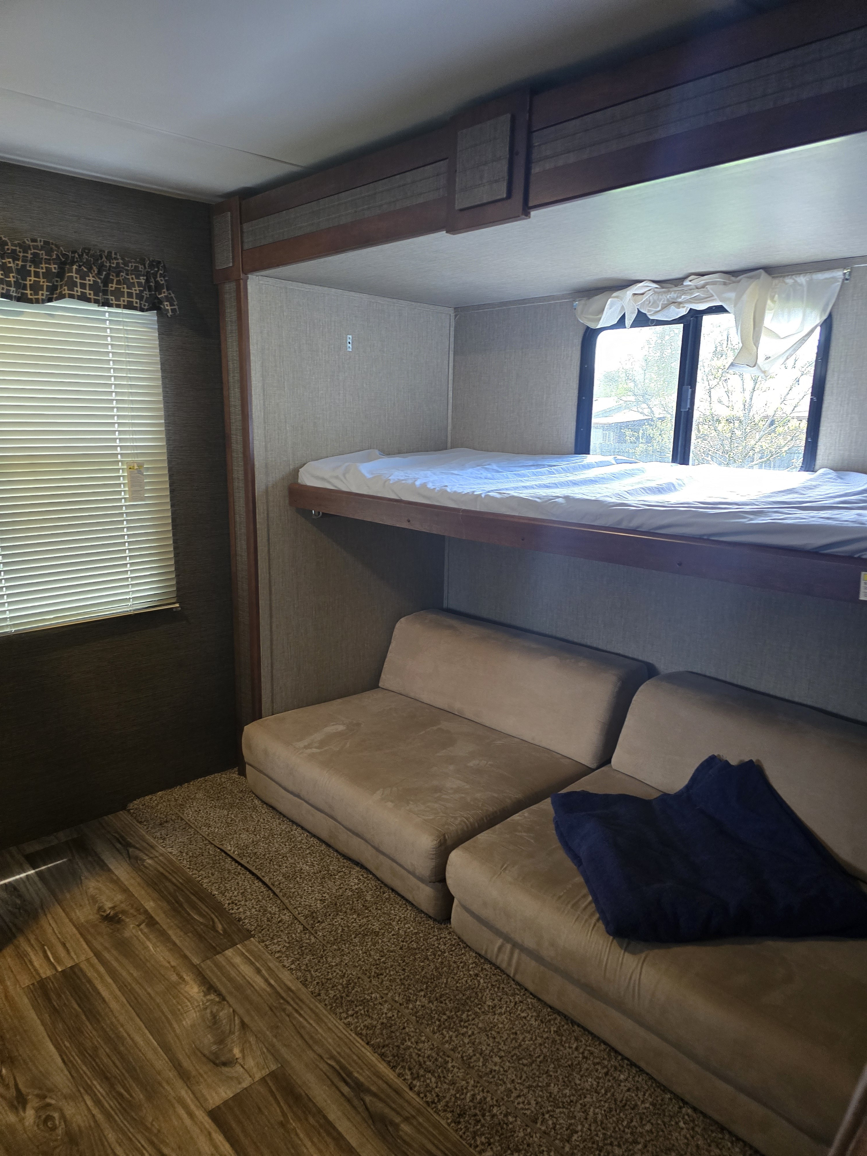 View inside an RV rental: a bunk bed with white sheet, modular tan sofas, and mixed wood/carpet flooring.. Keystone RV Passport Grand Touring 2017