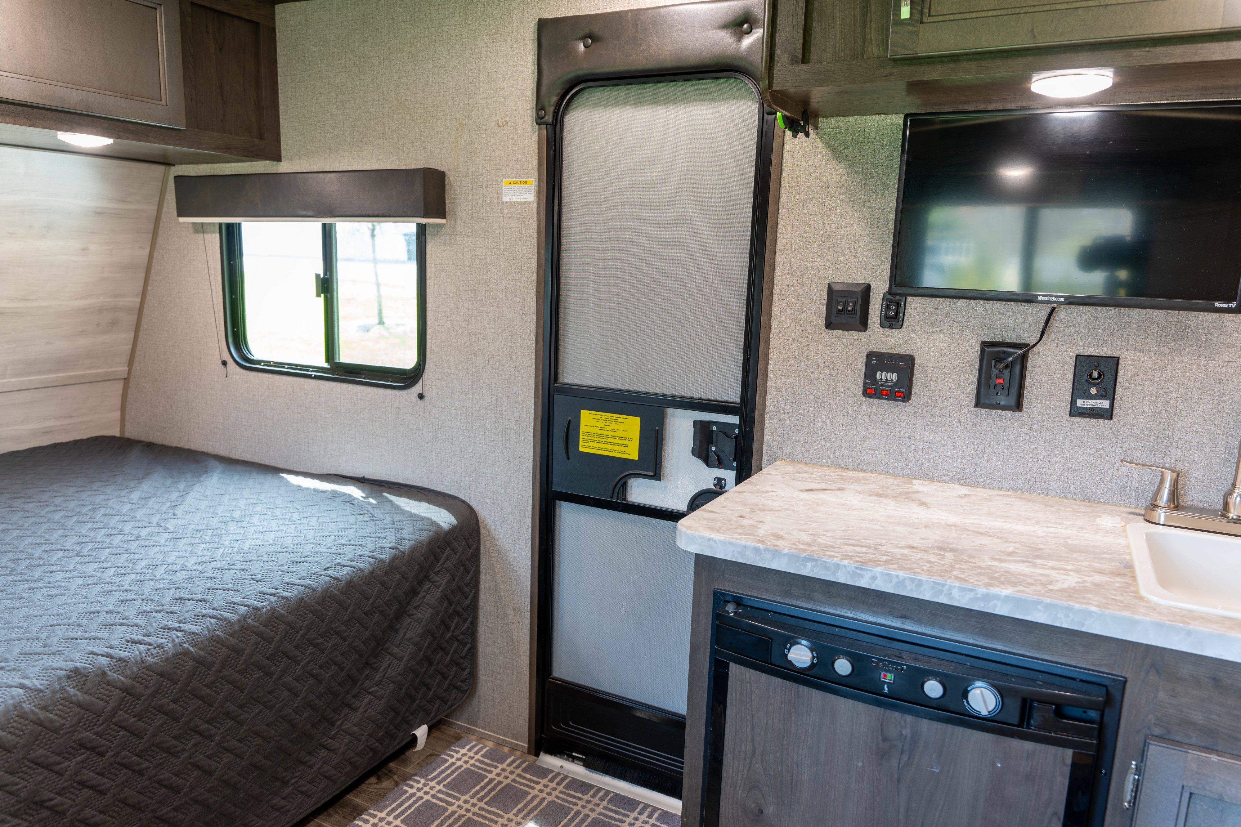 Explore this RV rental's inviting interior: a comfortable bed, functional kitchen with sink & fridge, and main entrance.. Jayco Jay Flight 2021