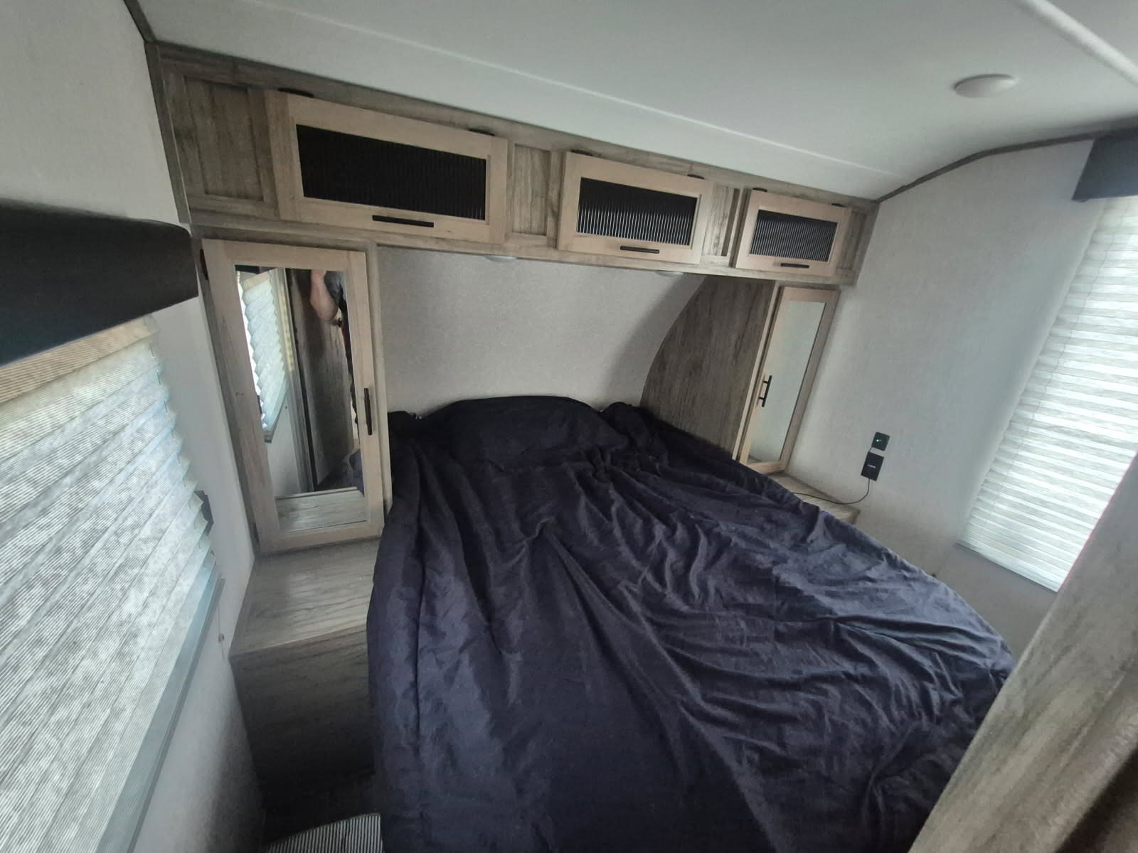RV rental bedroom: a dark bed, mirrored closets, overhead cabinets, and window blinds offer comfort for your travels.. Forest River Cherokee Alpha Wolf 2022