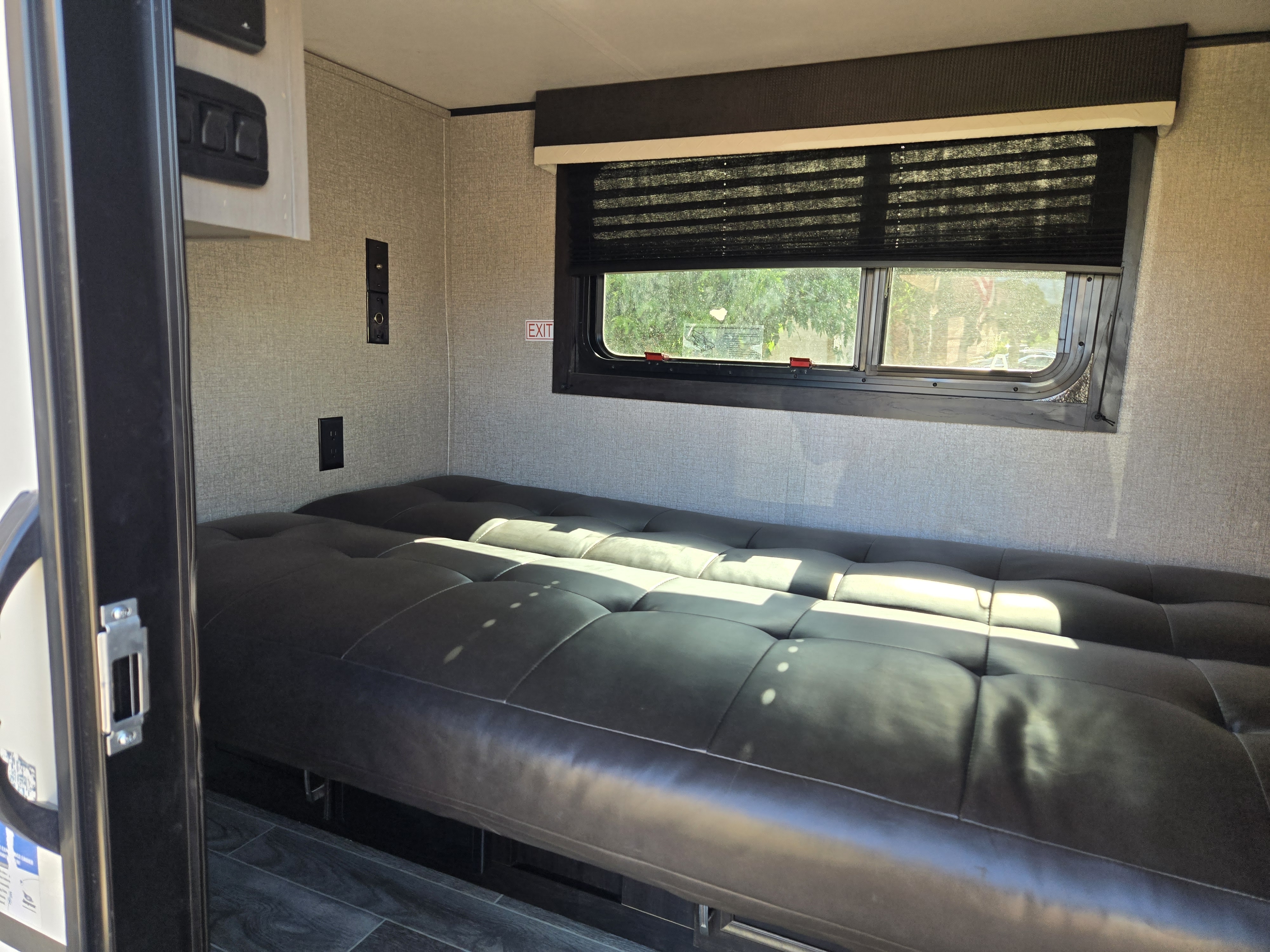 Sunlit RV rental interior: a comfortable black futon bed, large window with blinds, and practical wall outlets.. Jayco Jay Feather Micro 2021