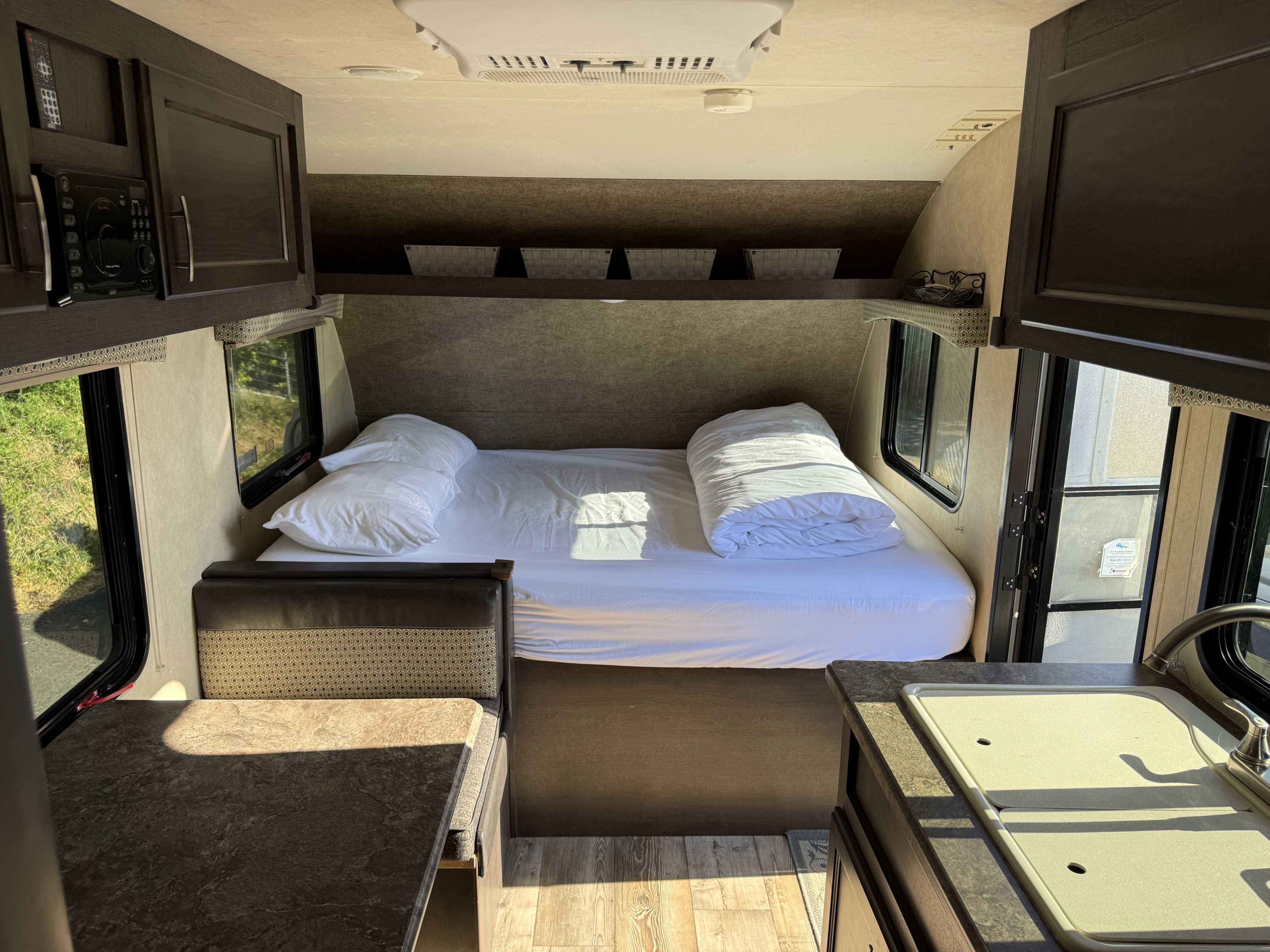 RV rental interior: bed with white linens, dinette, kitchen with sink, microwave, and overhead cabinets.. Forest River Sonoma 2019