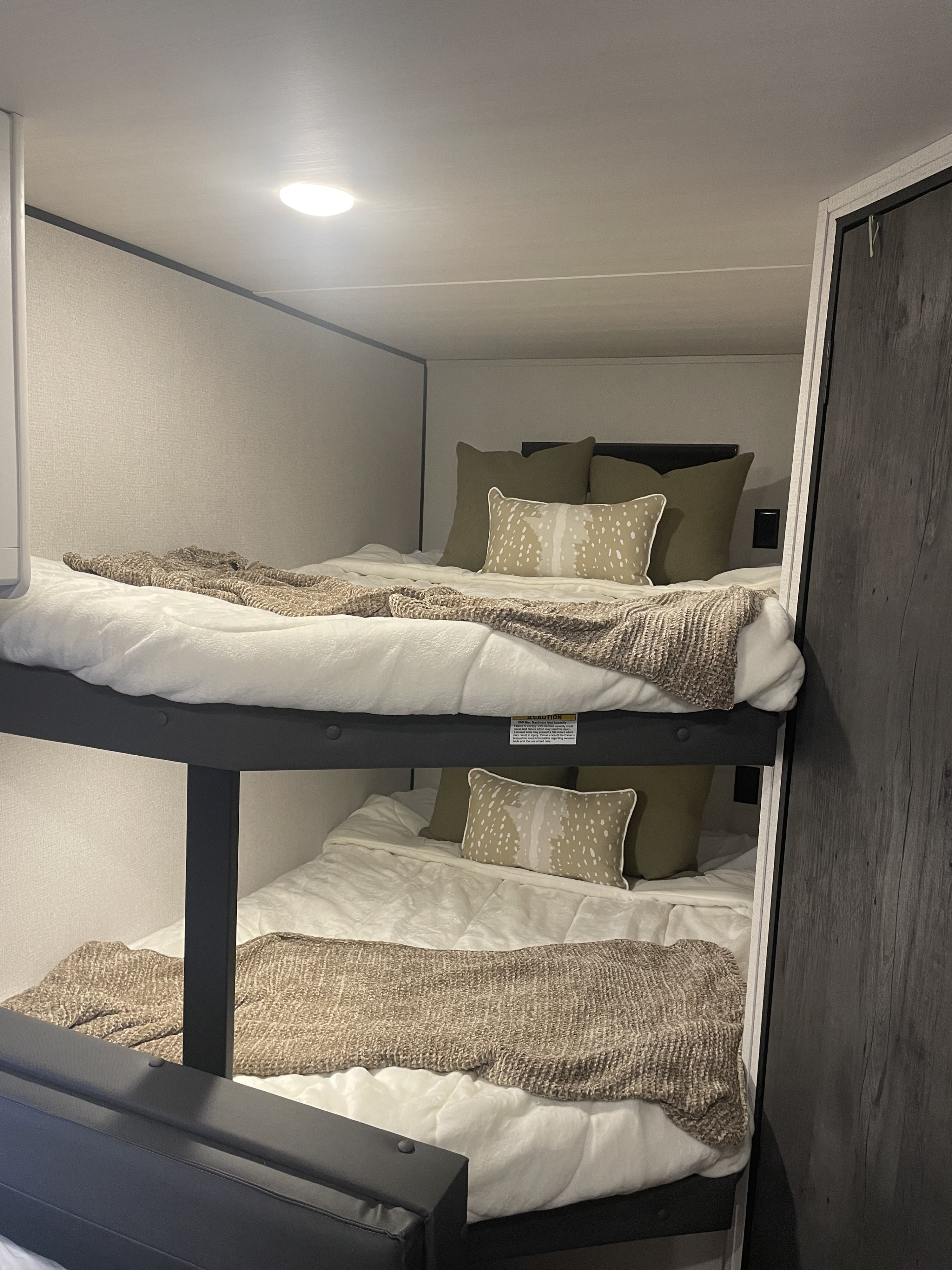 Inside an RV rental: comfortable bunk beds with white bedding, olive pillows, and a deer-print cushion. Ideal for family travel.. Keystone RV Hideout 2024