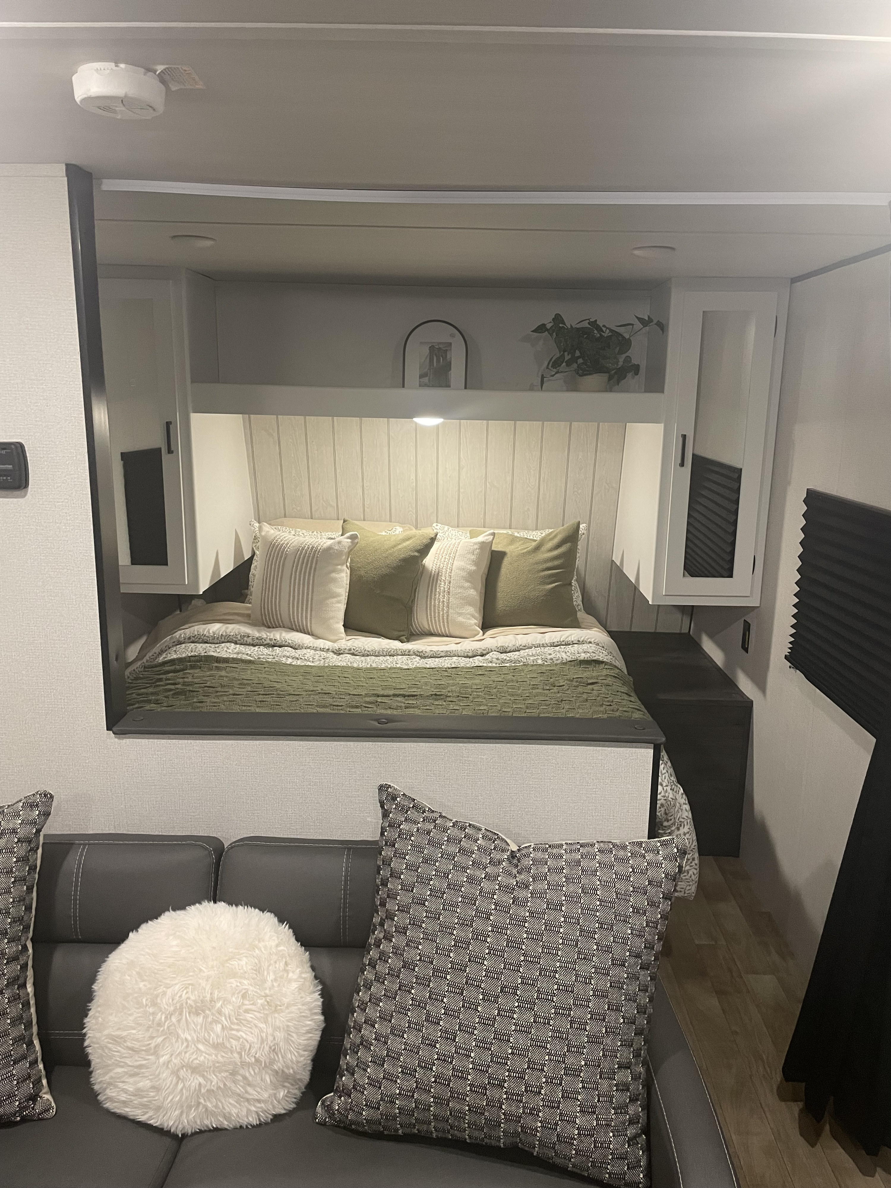 Inside an RV rental: a modern bed nook with green bedding, overhead cabinets, a small shelf, and a plush sofa.. Keystone RV Hideout 2024