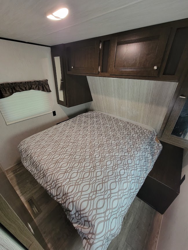 Cozy bedroom in an RV rental, featuring a queen bed with patterned comforter, overhead storage, and window.. Heartland Pioneer 2020