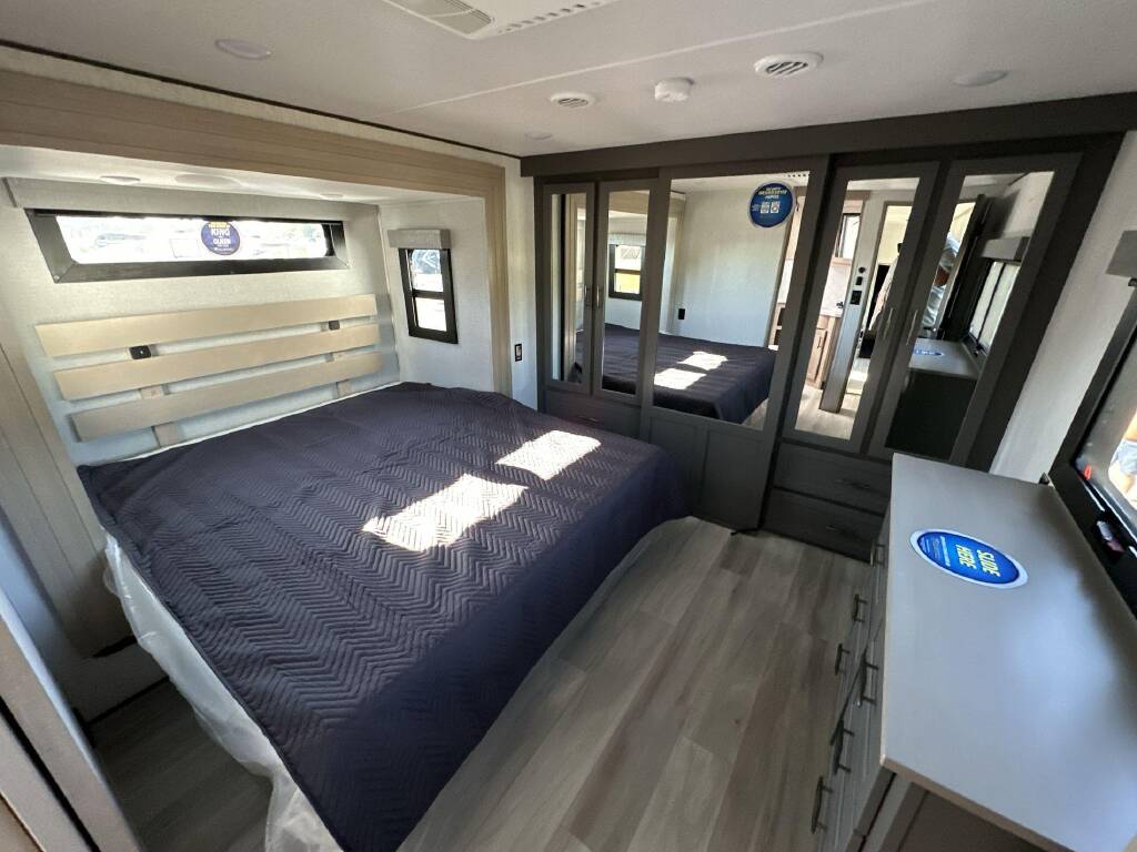 Comfortable RV rental bedroom featuring a king bed, mirrored storage, and windows. Ideal travel accommodation.. Grand Design Momentum 2024
