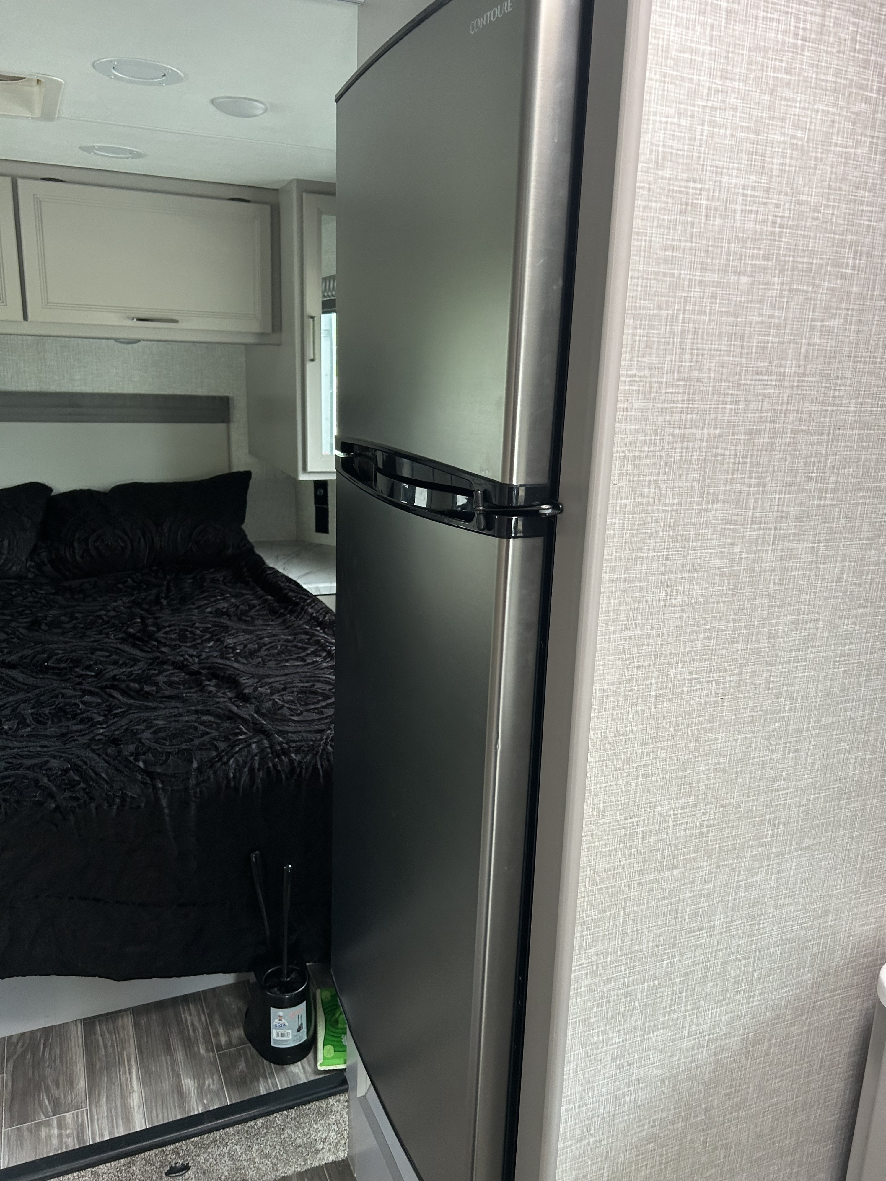 Compact RV rental interior featuring a cozy bedroom area with black bedding and a stainless steel refrigerator.. Thor Geneva 2024