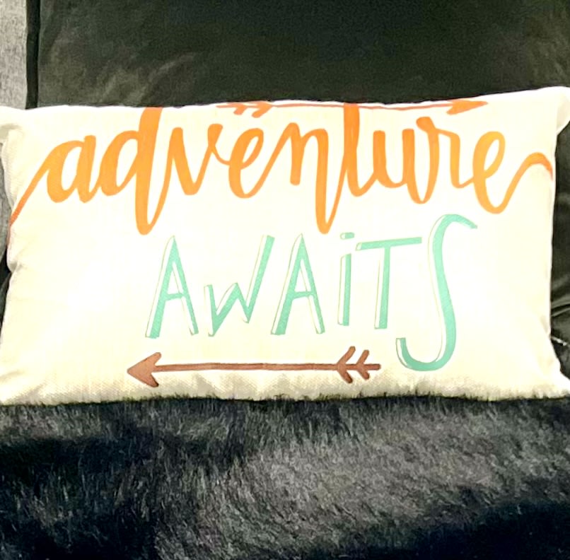 A white decorative pillow reads 'ADVENTURE AWAITS' in orange and teal, perfect for your next rv rental adventure!. Grand Design Imagine 2020