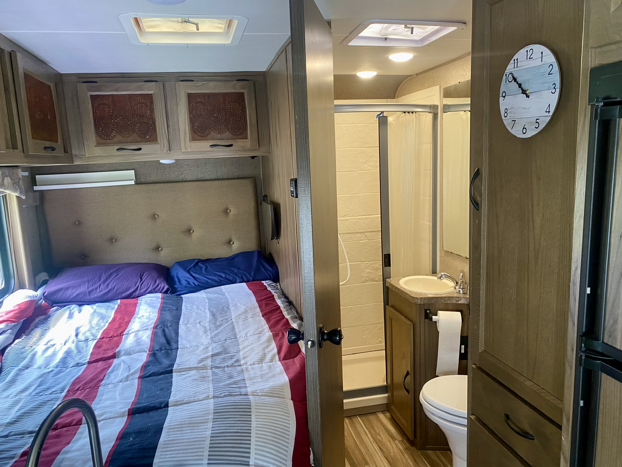 RV rental interior: a comfy bed with a striped comforter and adjacent compact bathroom.. Forest River Coachmen Freelander 2017