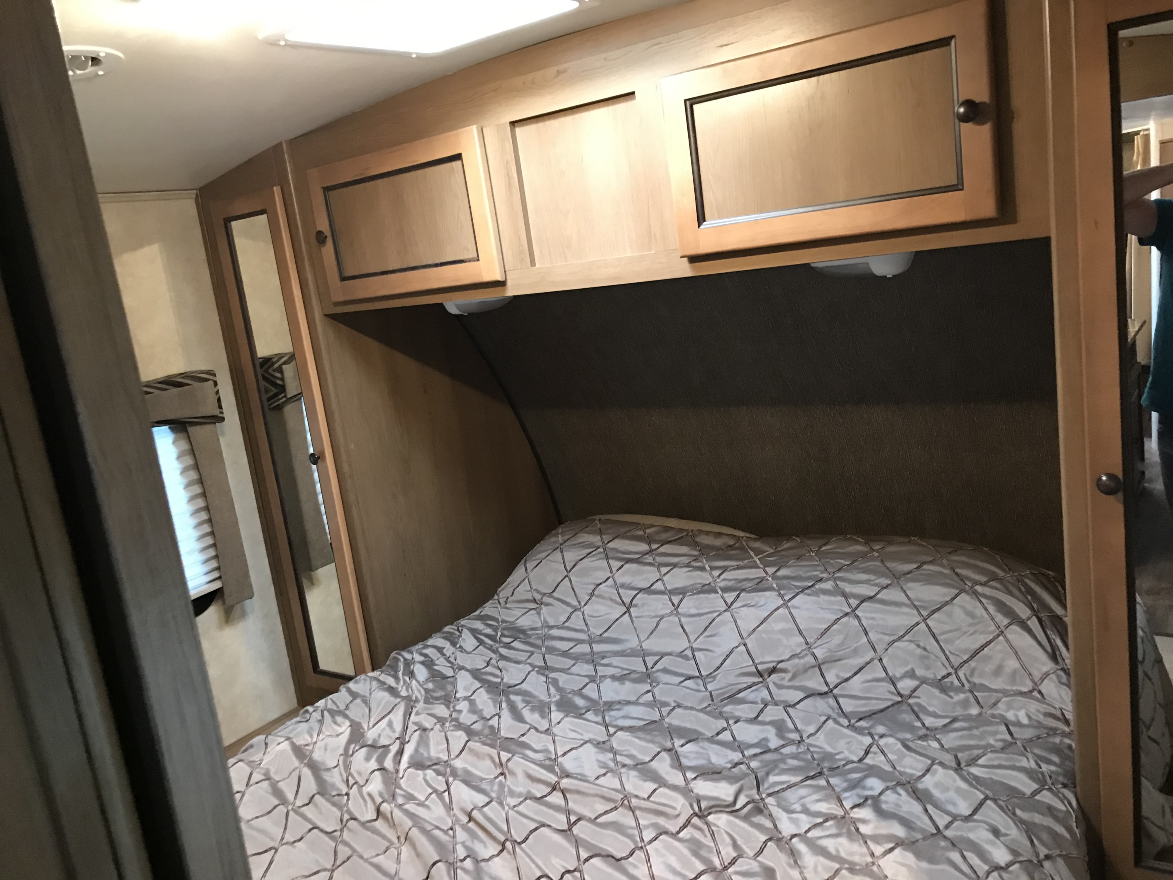 Cozy RV rental bedroom with a comfortable bed, overhead wood cabinets, and a mirrored closet door, ideal for travelers.. Cruiser RV Shadow Cruiser 2015