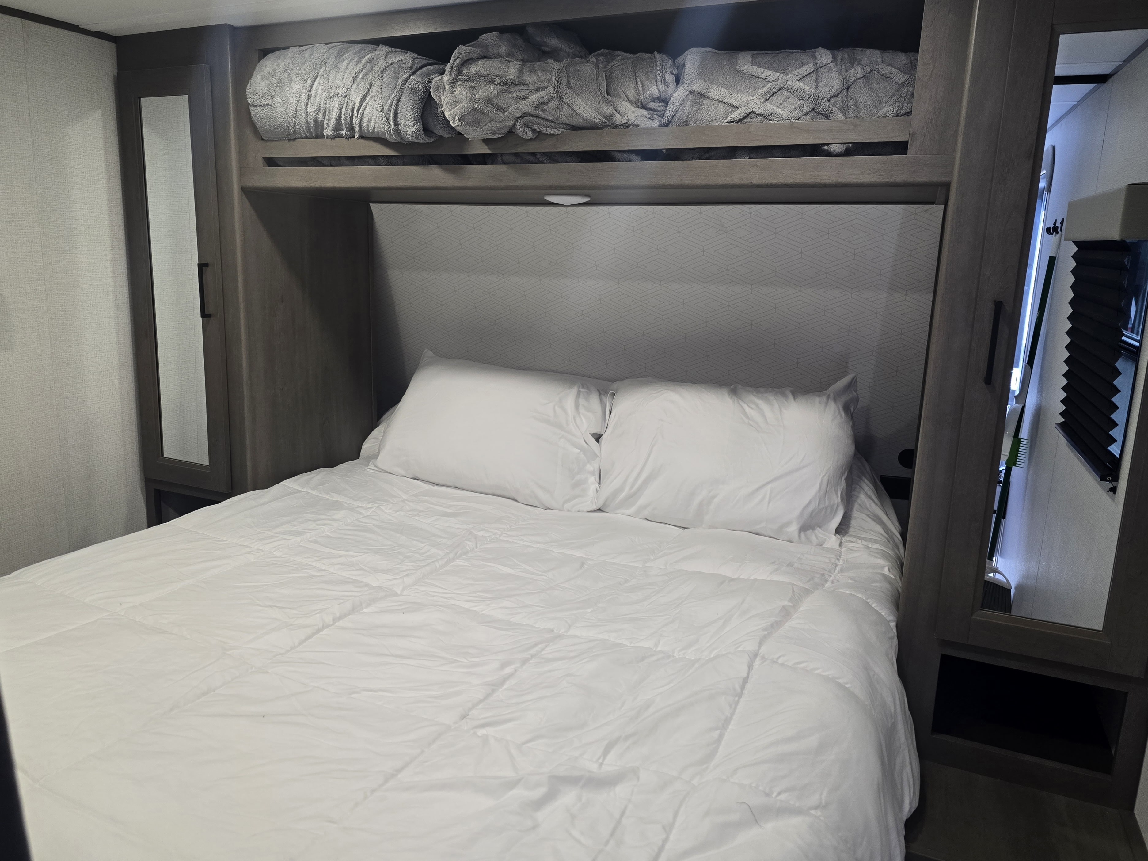 Cozy RV rental bedroom with a neatly made bed, white linens, and integrated storage including mirrored cabinets.. Grand design Transcend Xplor 2025