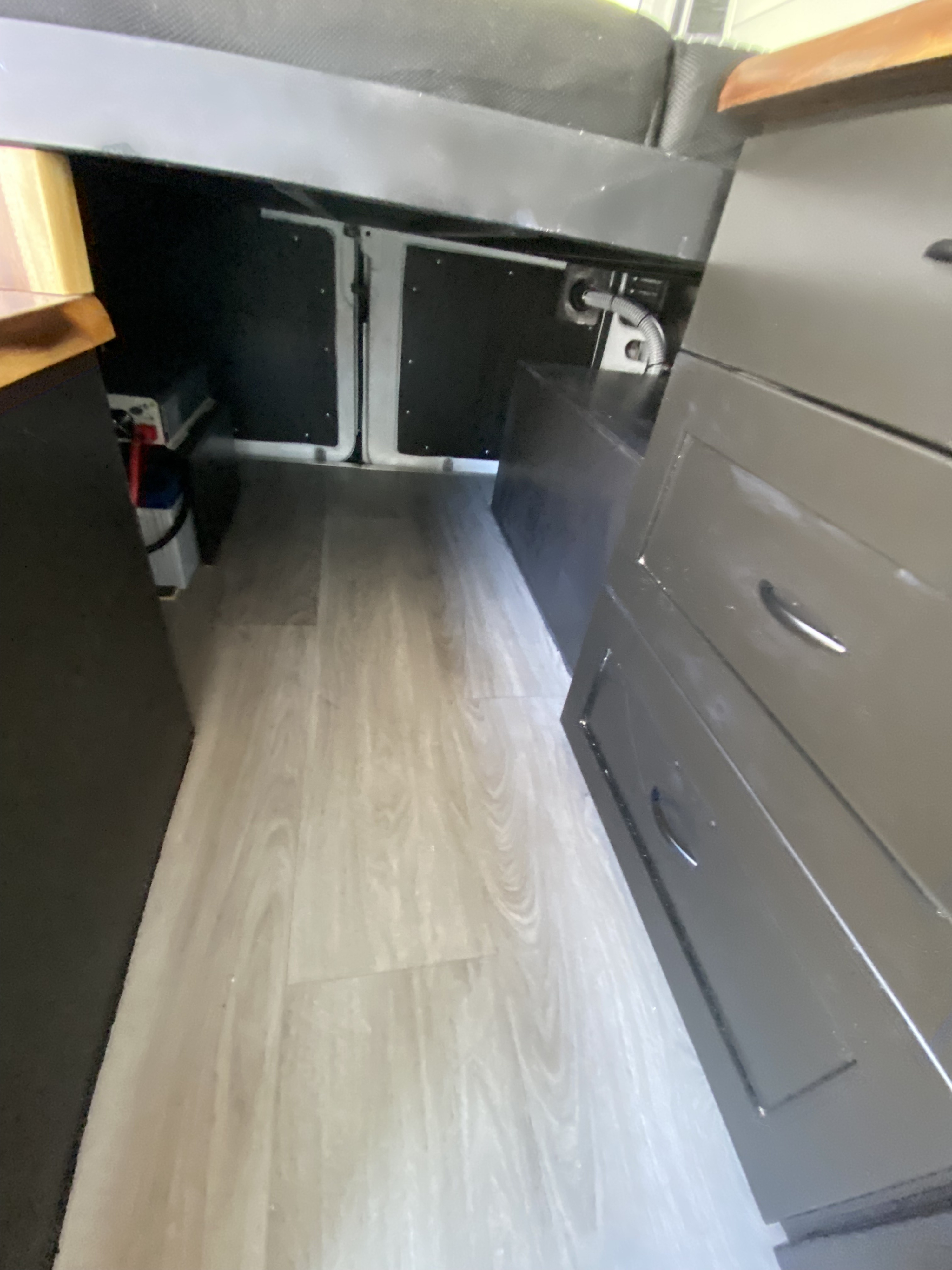 RV rental: Interior view showing light wood-look flooring, under-bed storage with batteries, and a dark cabinet with drawers.. Custom Ram Promaster 1500 2017