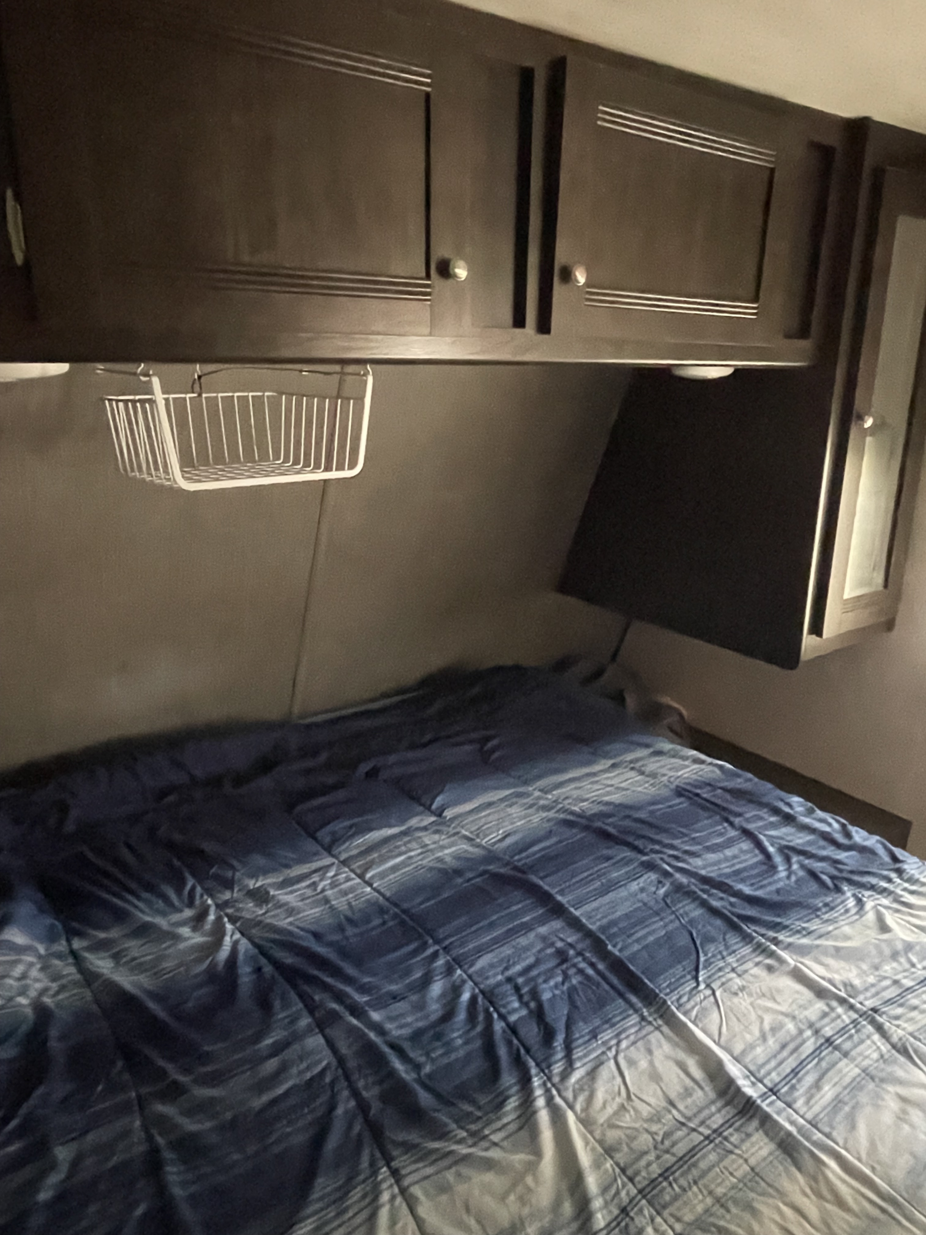 Cozy RV rental bedroom with dark wood cabinets, a blue striped bed, and a wall-mounted TV. Compact and functional.. Heartland RVs Trail Runner 2019