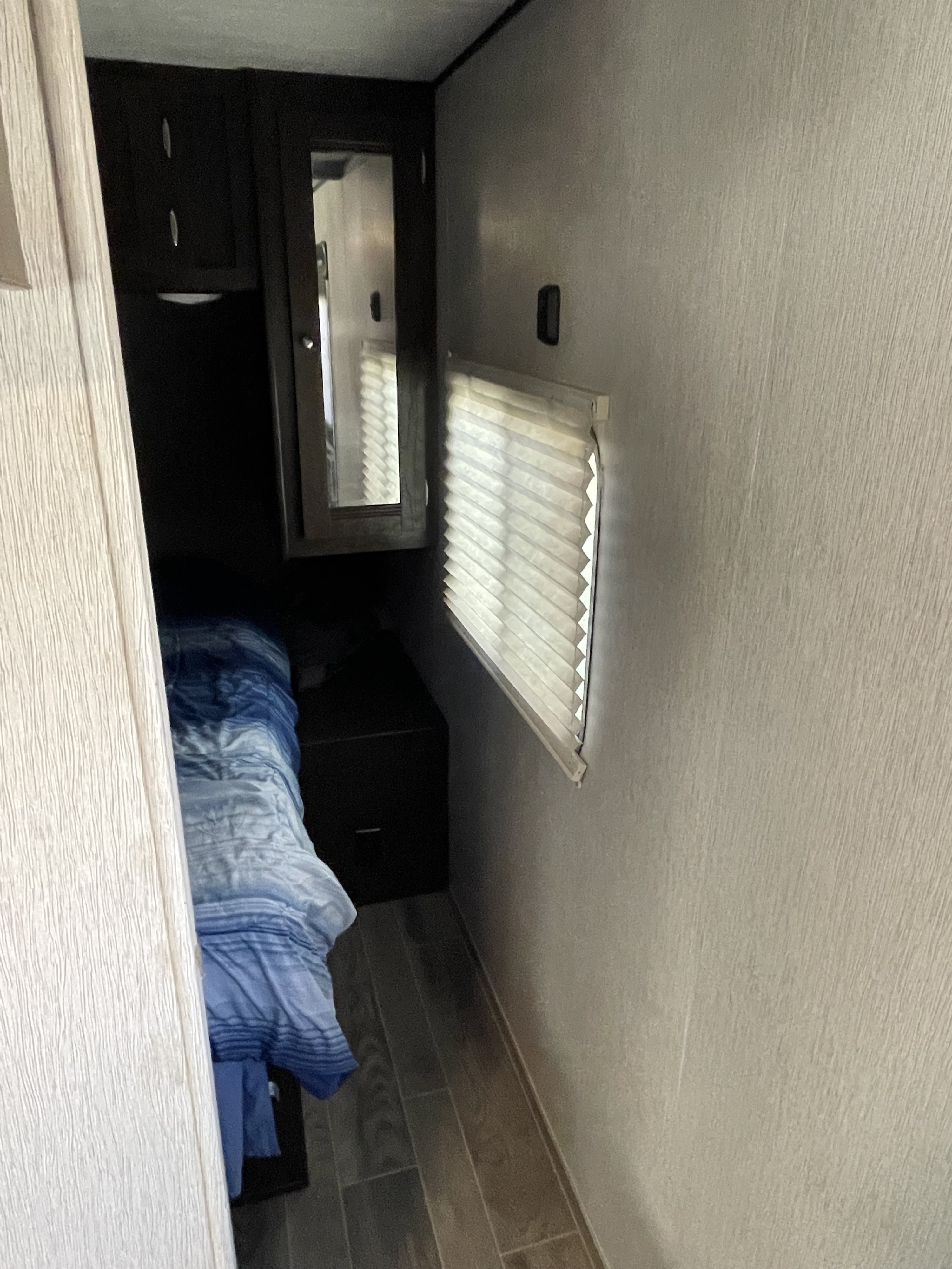 Compact RV rental bedroom: bed with blue bedding, mirrored wardrobe, and window with pleated blinds.. Heartland RVs Trail Runner 2019