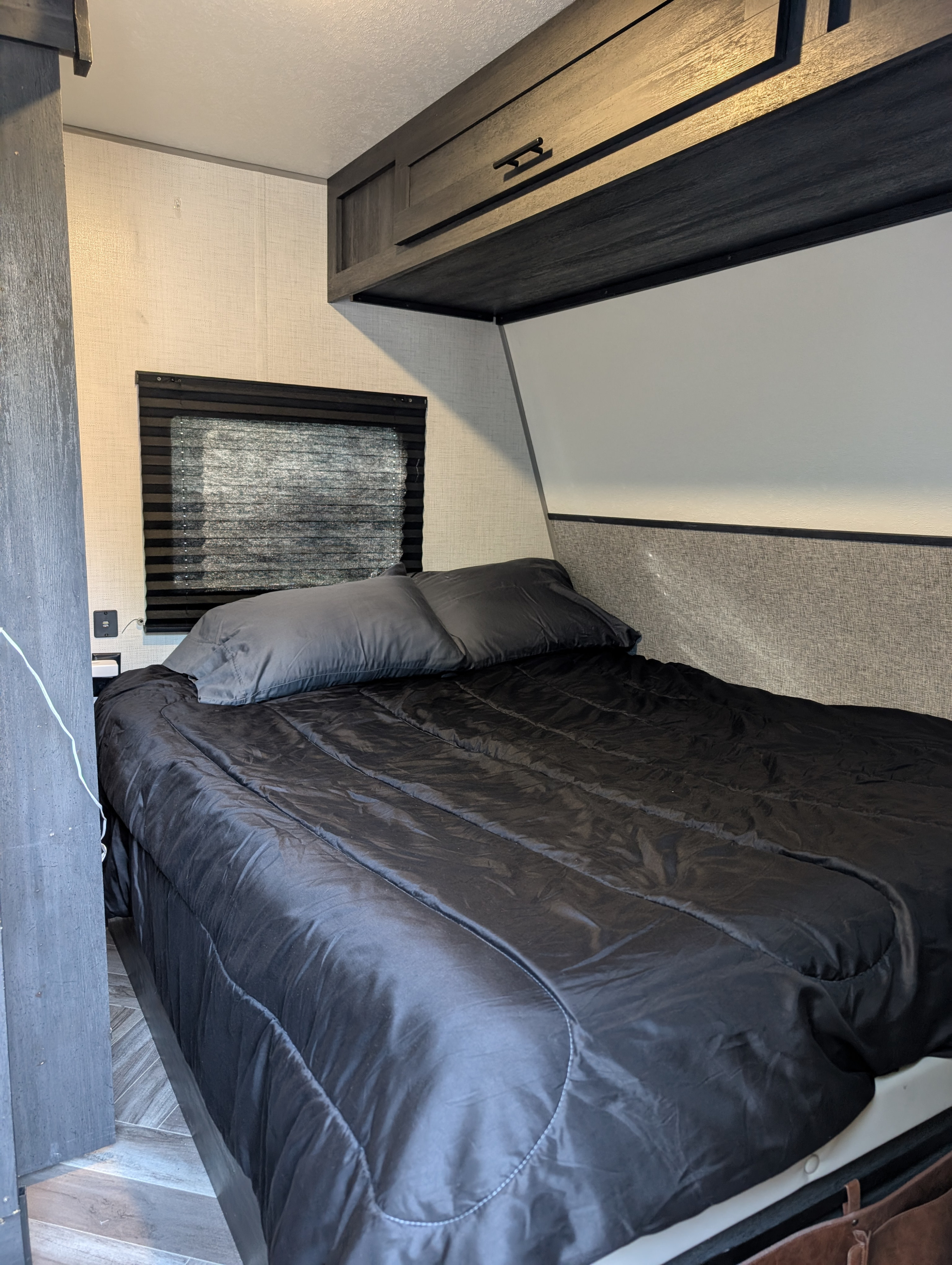 Cozy RV rental bedroom with a dark bed, window blinds, & overhead cabinets for comfortable travels.. Forest River 2700TH 2021