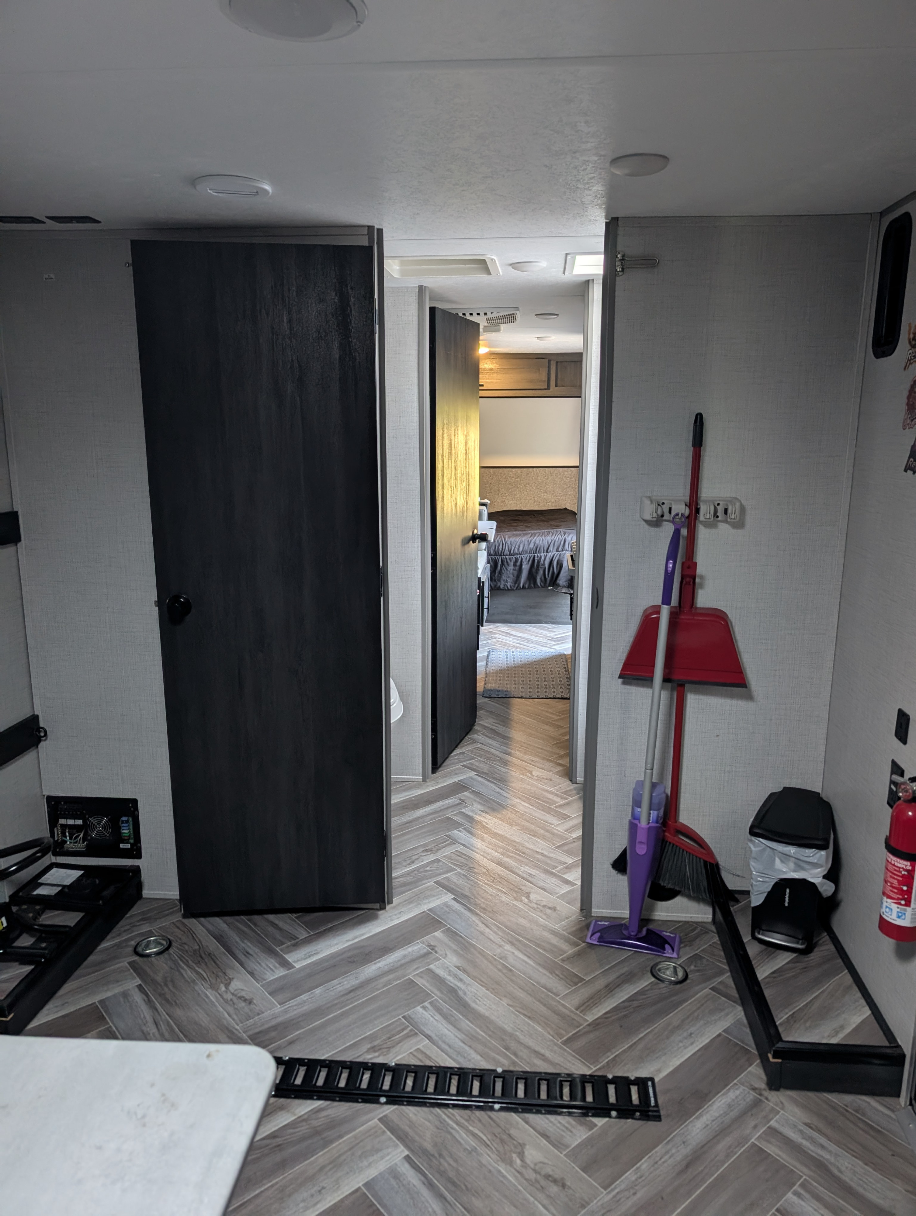 RV rental interior: herringbone flooring leads to a cozy bedroom. Cleaning tools, fire extinguisher, and utility panel for practical living.. Forest River 2700TH 2021