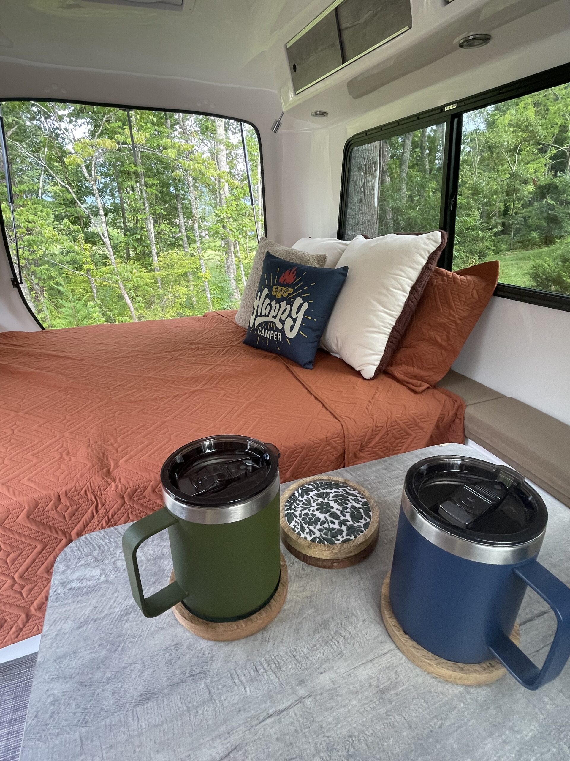 RV rental: Cozy camper interior with a bed by scenic windows, forest views, and morning mugs on a table.. Happier Camper HC1 2022