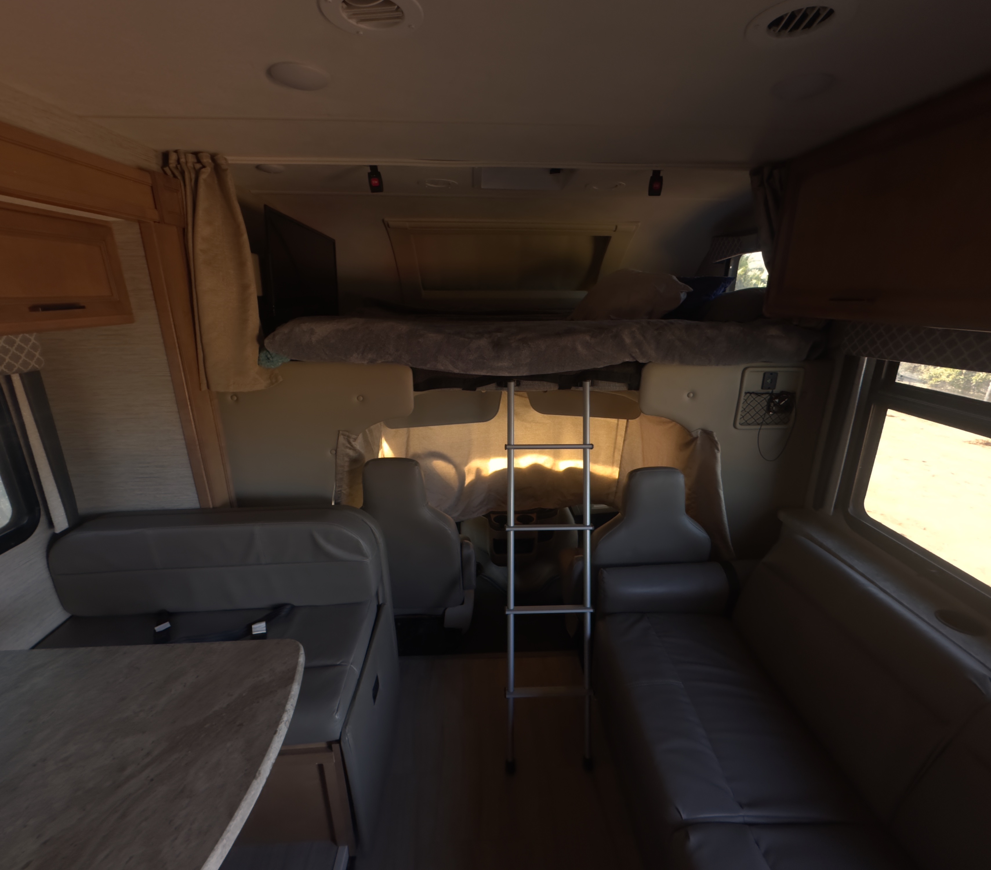 RV rental interior: bunk bed with ladder, dinette, and sofa. Sunlight fills this cozy mobile living space.. Thor Quantum 2021
