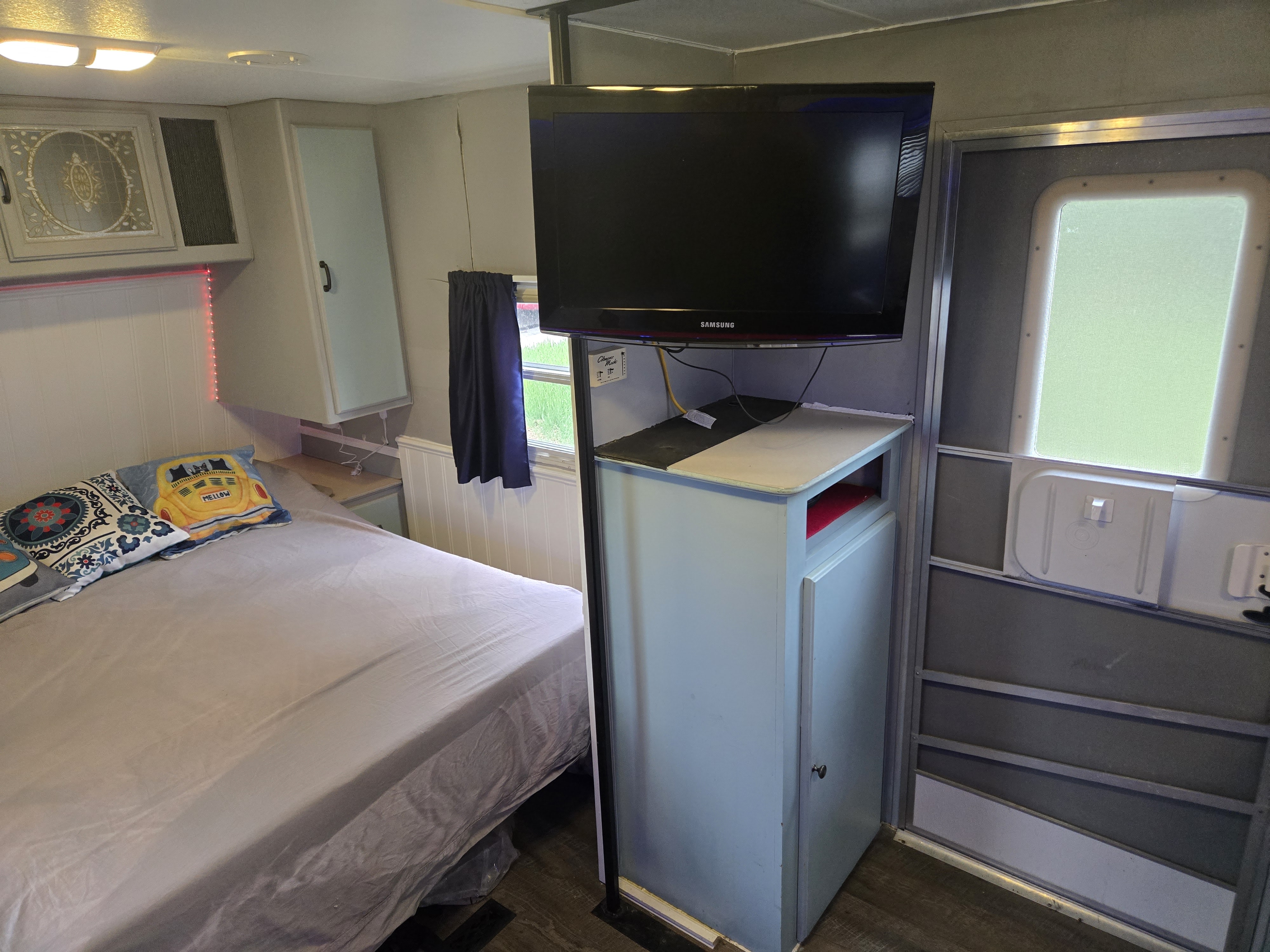 RV rental interior: cozy bedroom with a bed, mounted TV, and built-in storage. Features a side door.. Fleetwood Mallard 2004