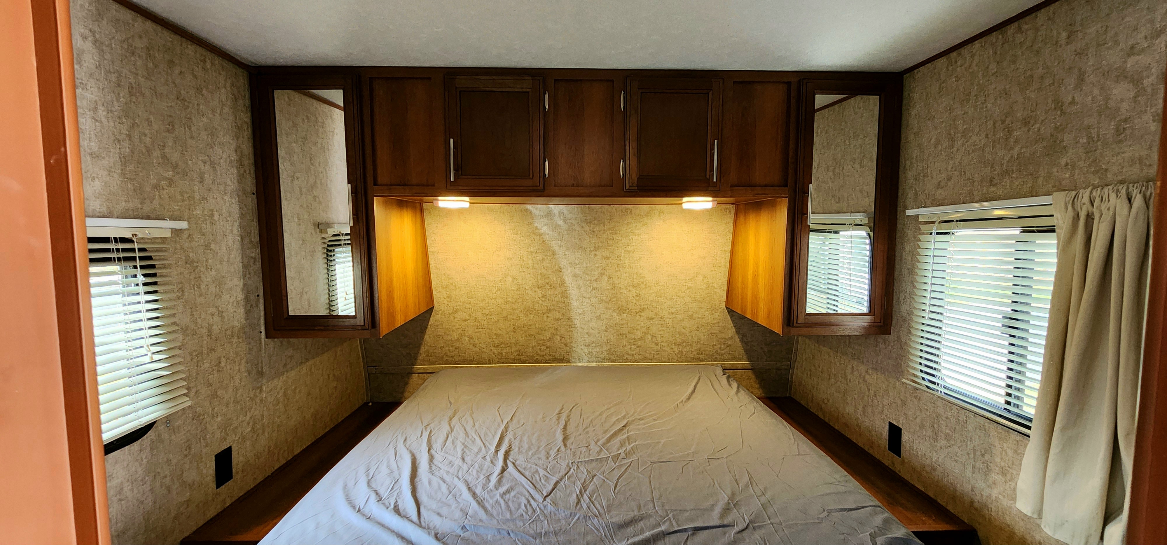 This RV rental features a cozy bedroom with an inviting bed, practical overhead storage cabinets, and side windows with blinds.. Avenger ATI 2018