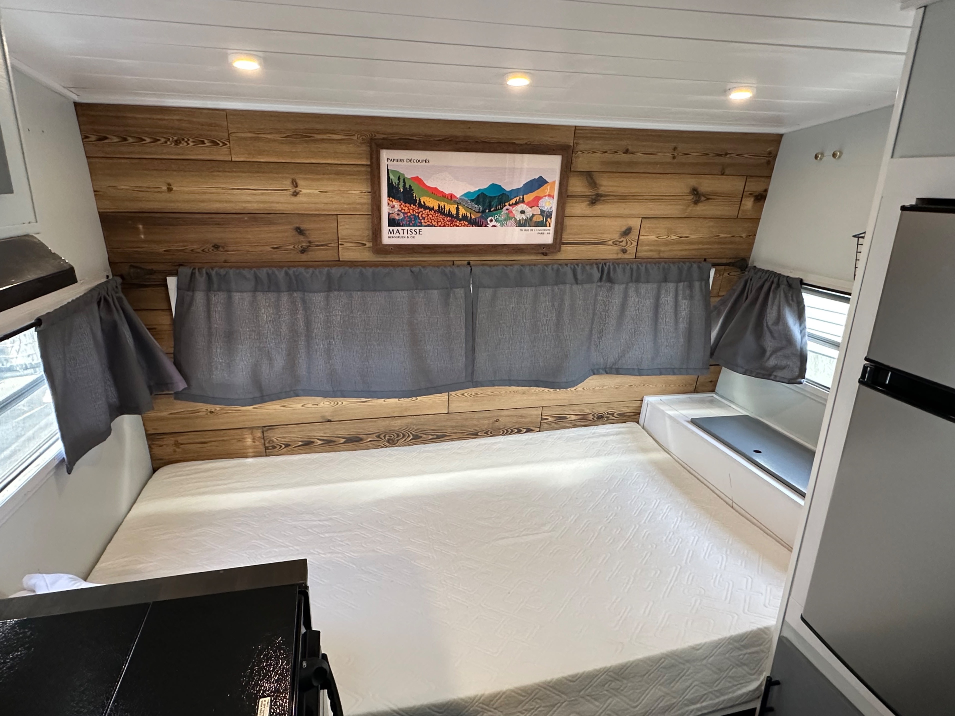 Discover this comfortable RV rental bedroom, featuring a large mattress, rustic wood-paneled walls, and soft lighting.. Cabin Trailer Skipper 1976