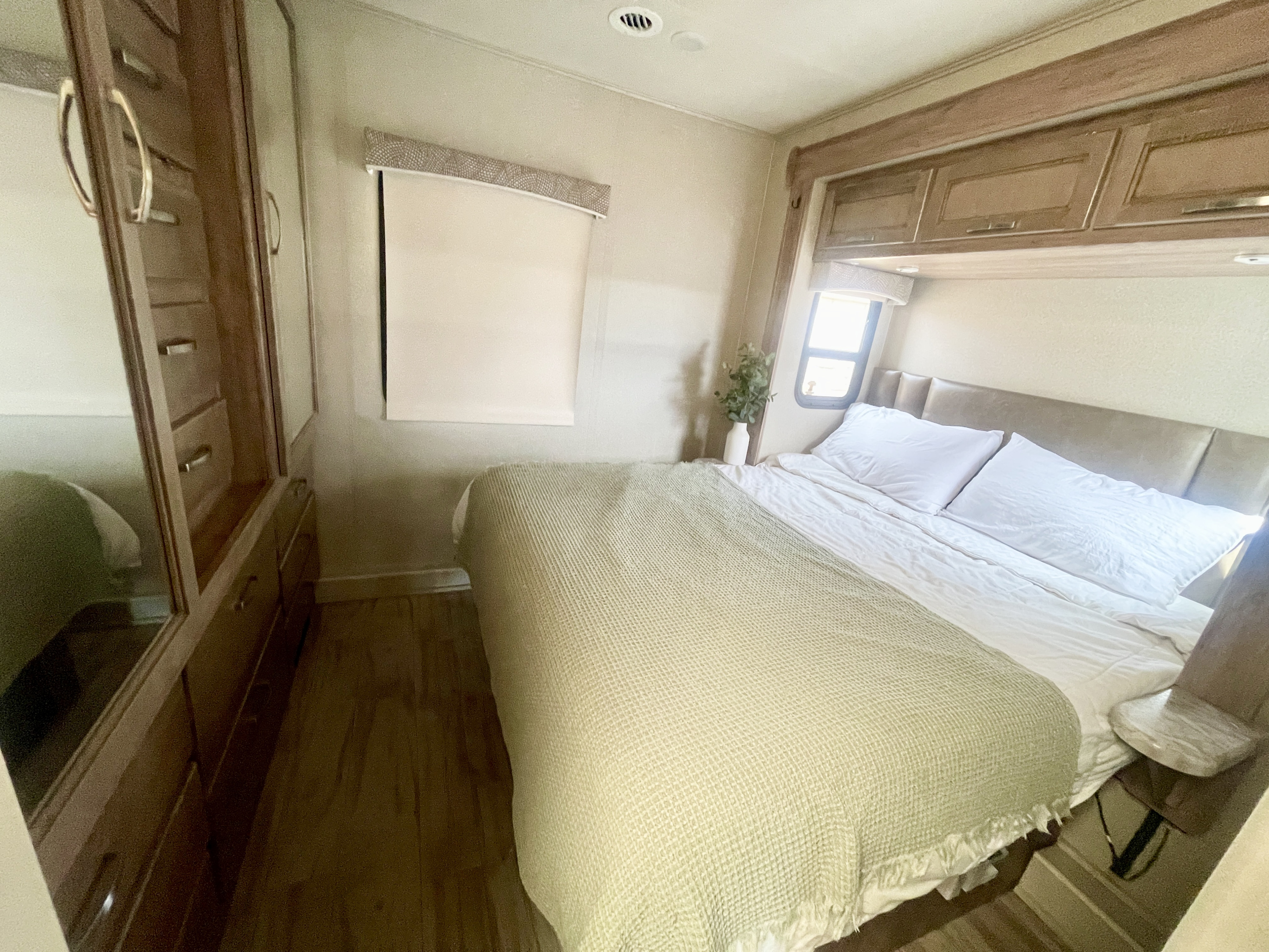 Cozy RV rental bedroom with a plush bed, upholstered headboard, overhead cabinets, and mirrored wardrobe.. Entegra Coach Vision 31V 2019