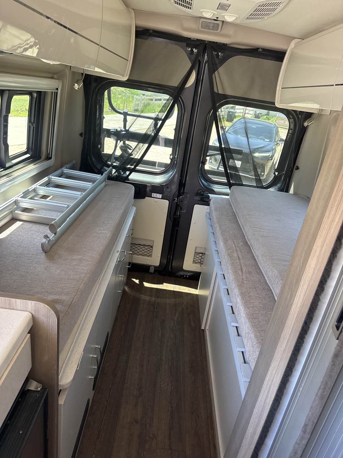 Inside an RV rental: view of twin beds, central aisle, and storage, looking towards bug-screened rear doors.. Thor Tellaro 2022